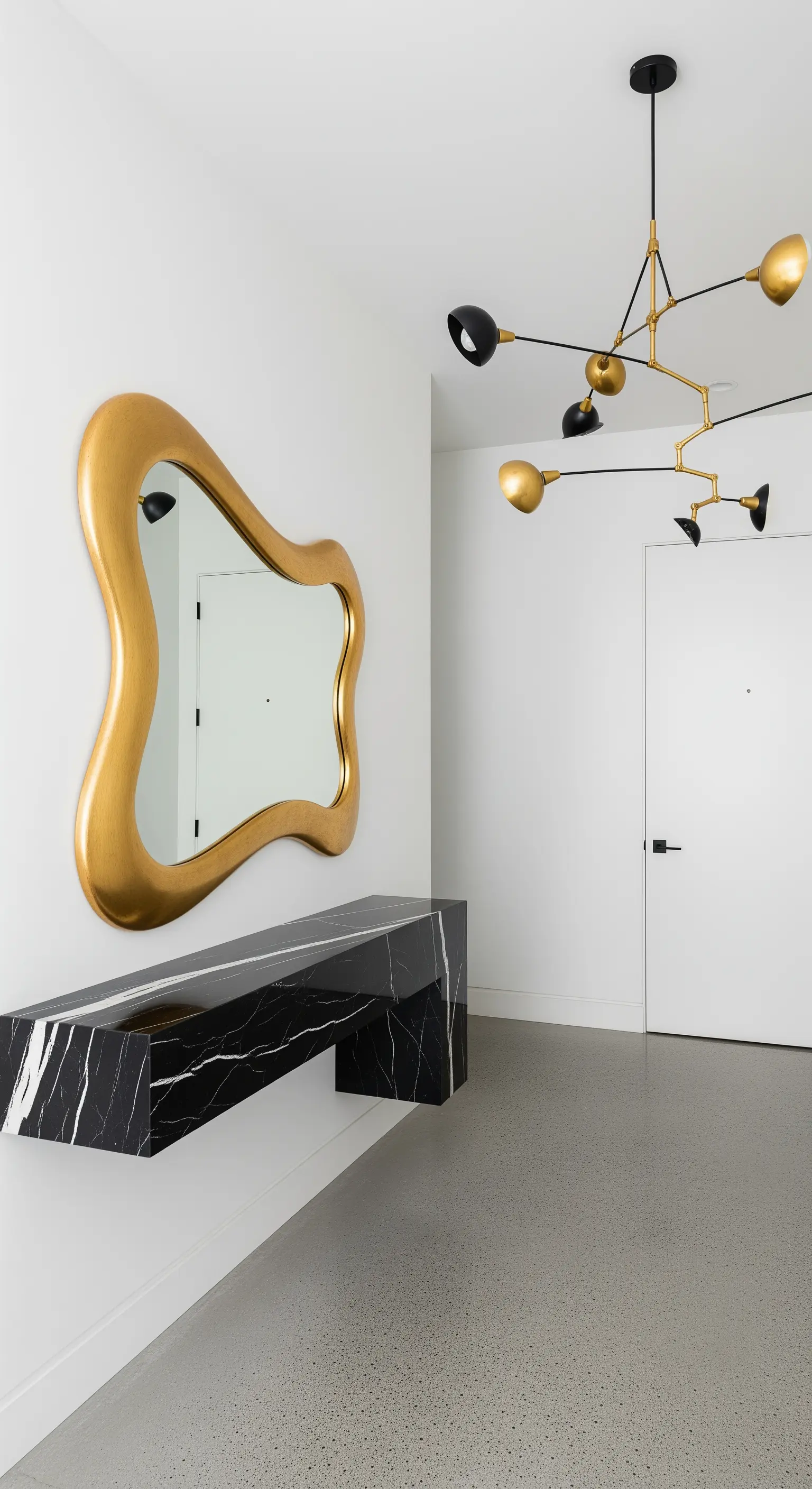 Ingresso minimalista con specchio dorato asimmetrico e consolle sospesa in marmo nero.