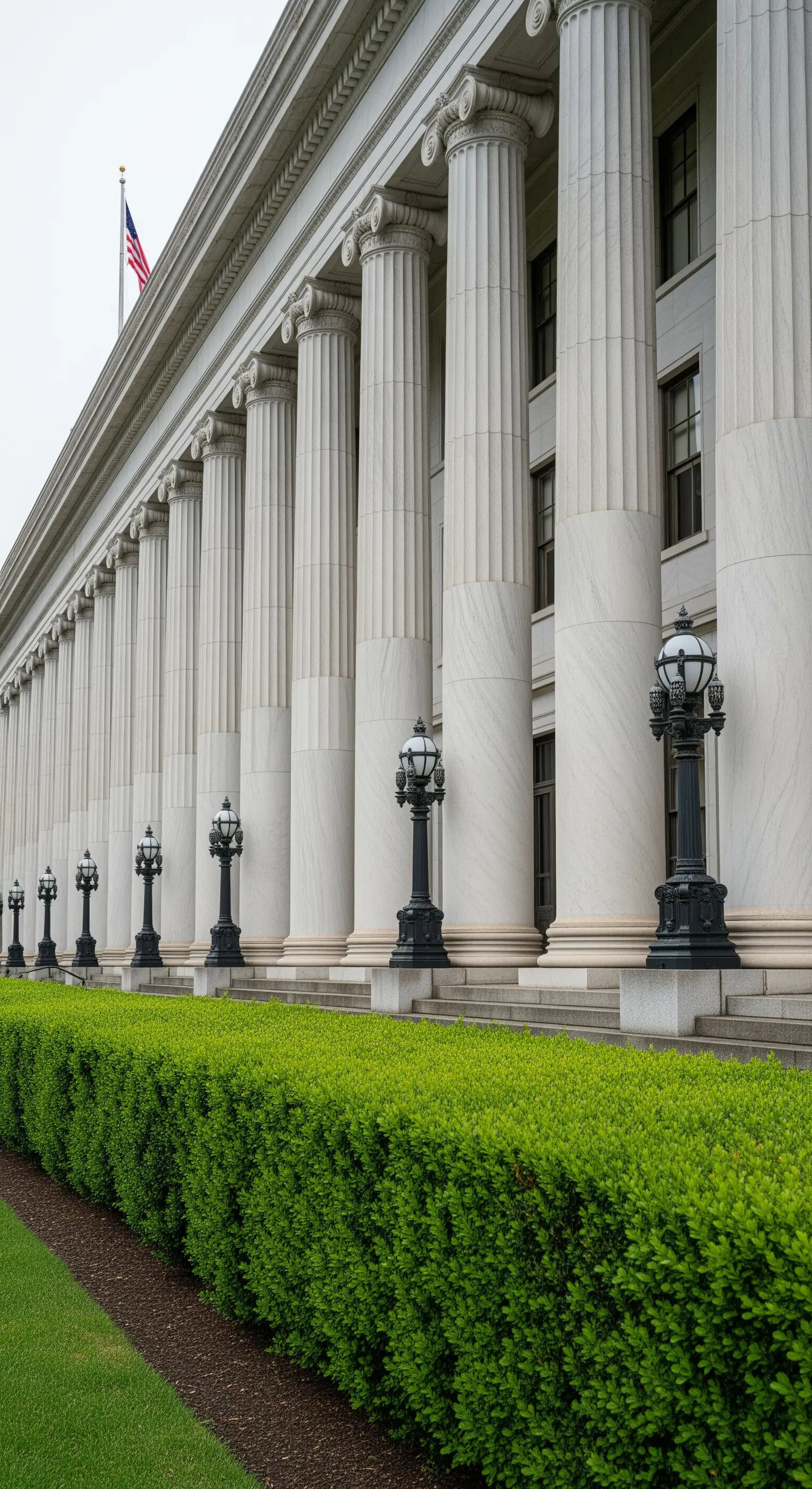 Lunga e imponente colonnata di un edificio classico, affiancata da una siepe verde perfettamente potata