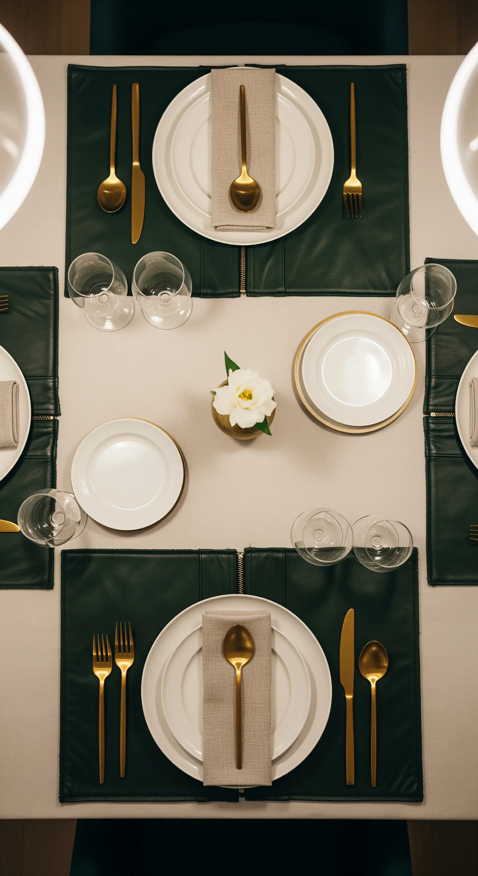 Tavola apparecchiata con tovagliette in pelle verde scuro, posate dorate e piatti bianchi.