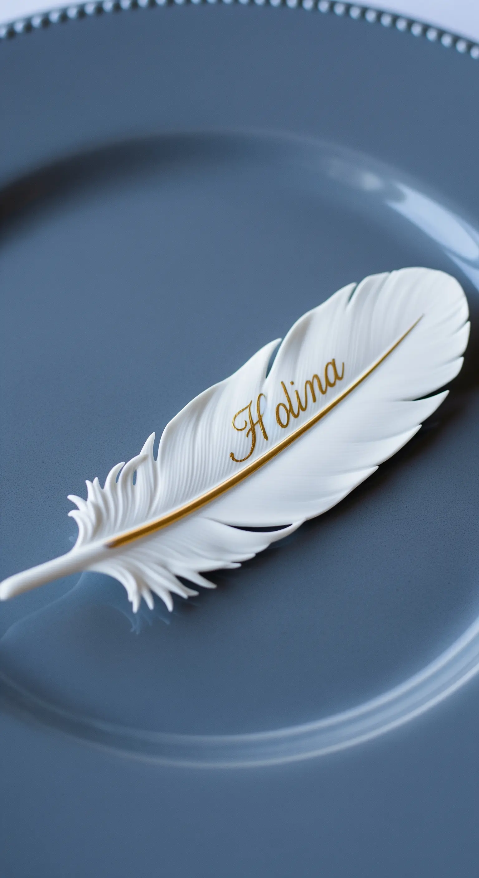 Piuma bianca con il calamo dorato e un nome scritto in oro, su un piatto grigio scuro.