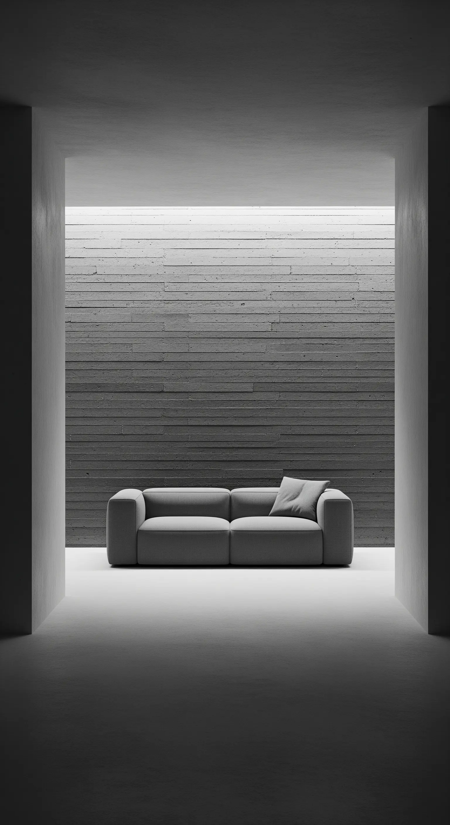 Spazio minimalista in cemento con un singolo divano grigio e illuminazione lineare a soffitto