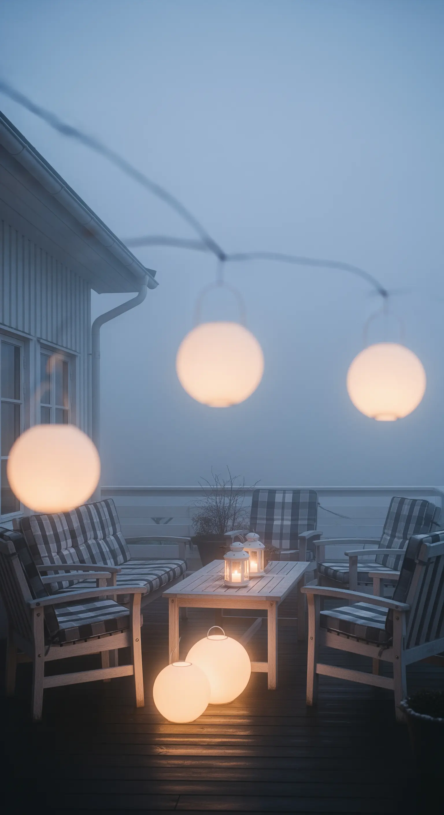 Patio avvolto nella nebbia, illuminato da una ghirlanda di luci sferiche e lanterne a terra.