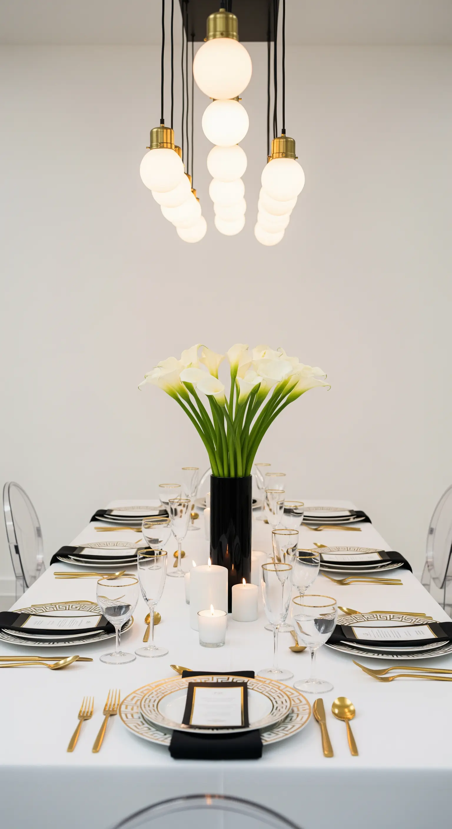 Tavola moderna in bianco, nero e oro con calle bianche e sedie trasparenti.