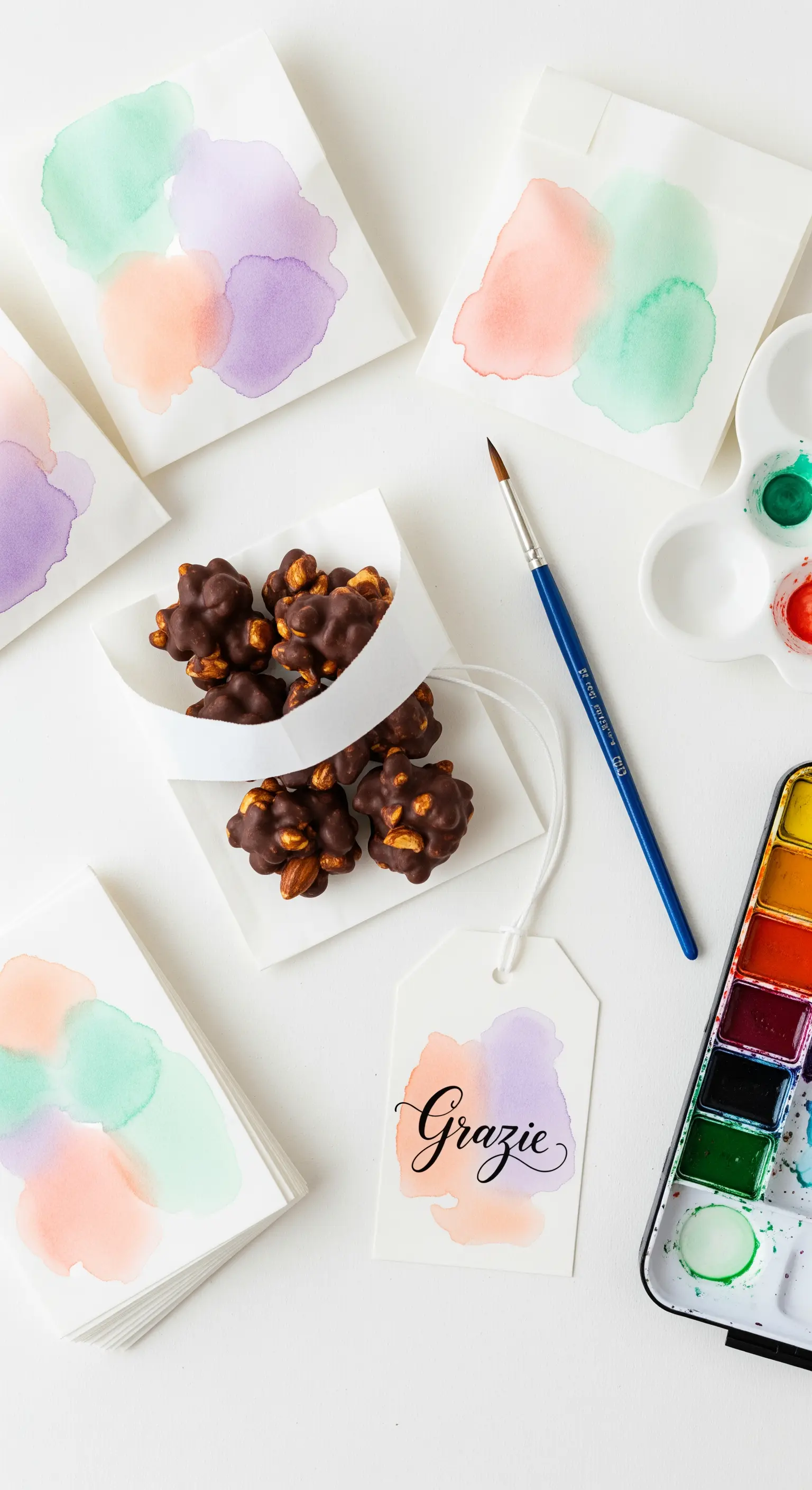 Bustine di carta e etichette decorate con macchie di acquerello in toni pastello.