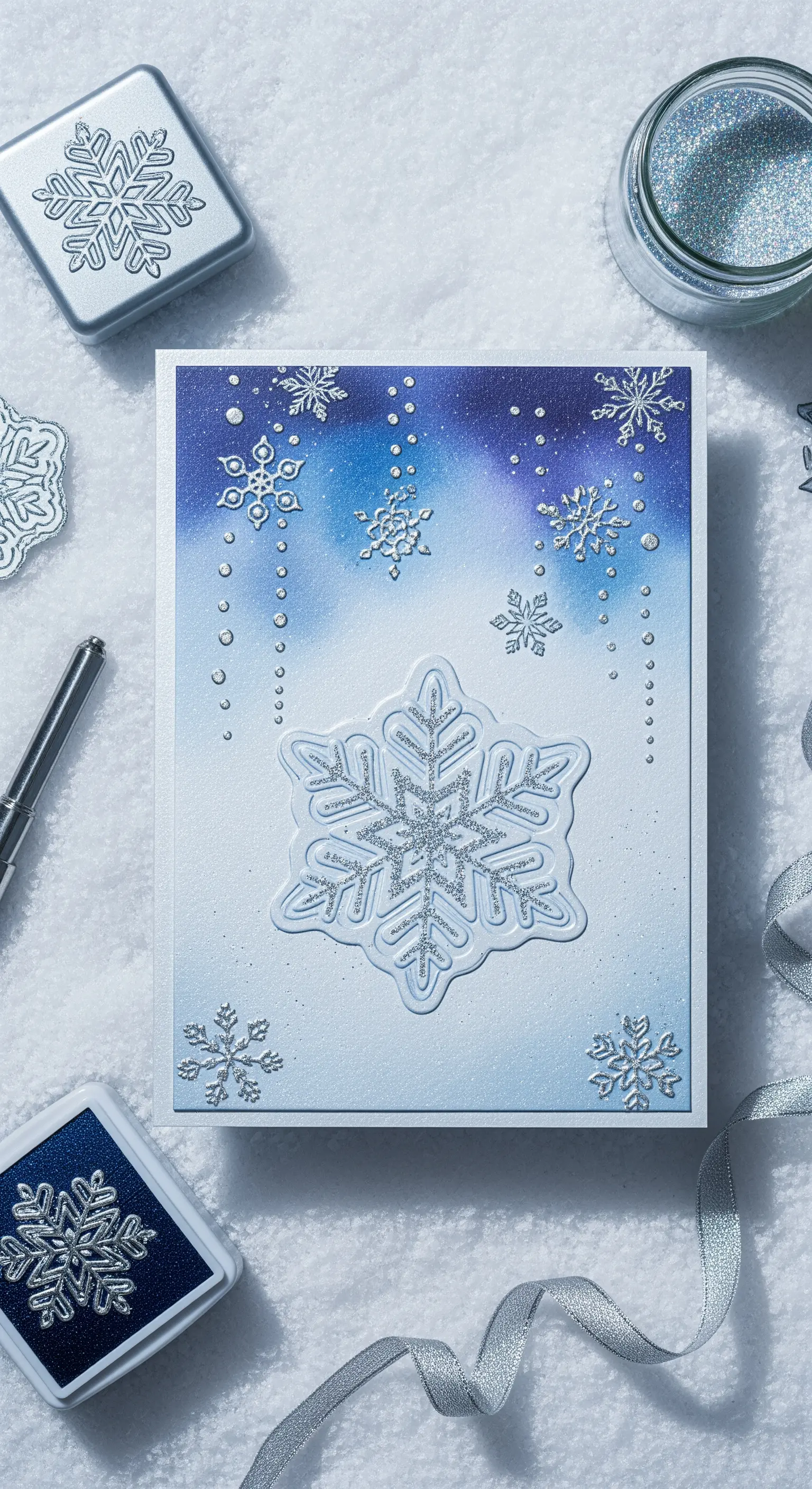 Biglietto invernale con fiocchi di neve in rilievo e glitterati su sfondo blu sfumato.