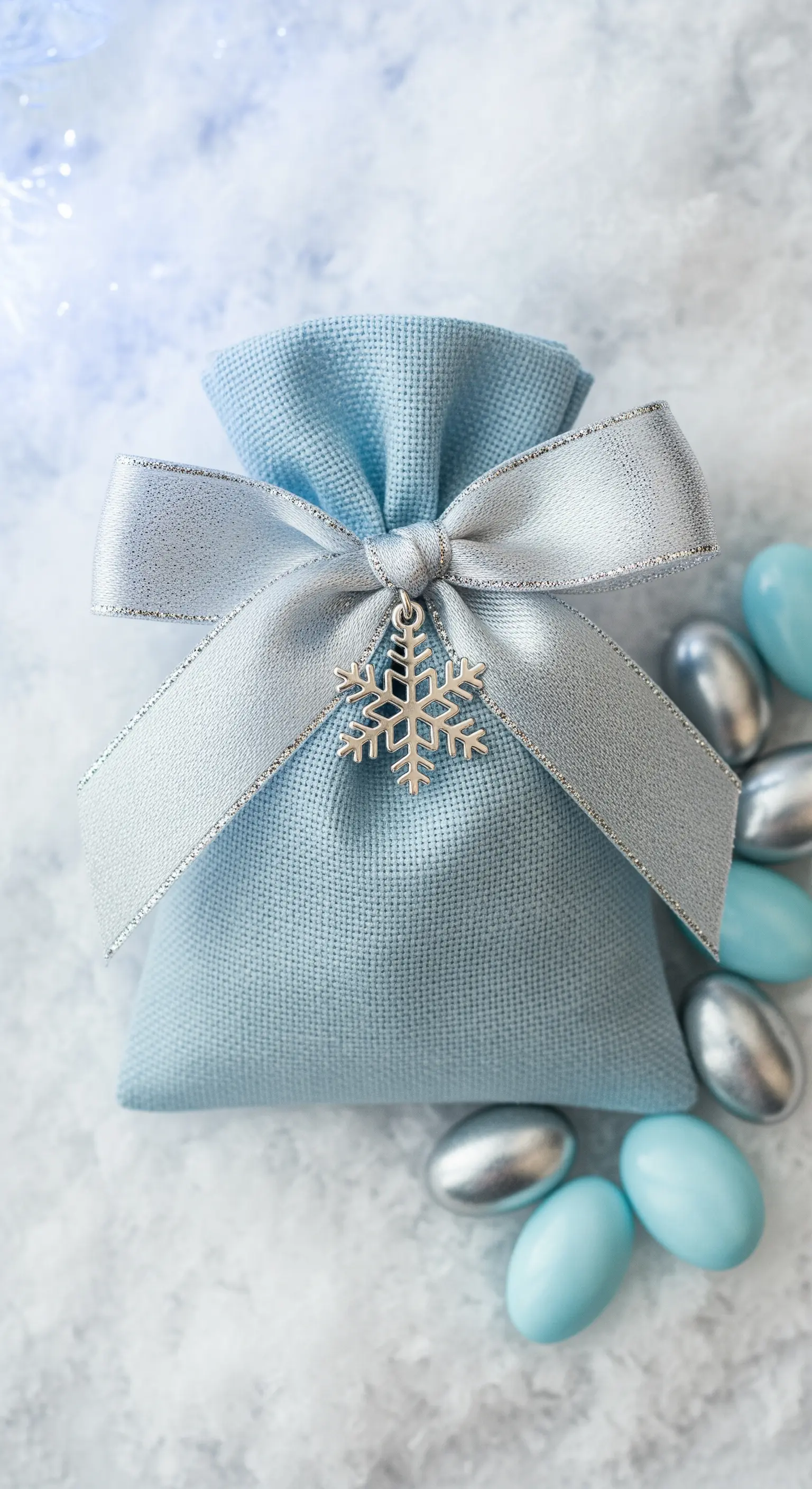 Bomboniera azzurra con nastro argentato e ciondolo a forma di fiocco di neve, circondata da confetti.