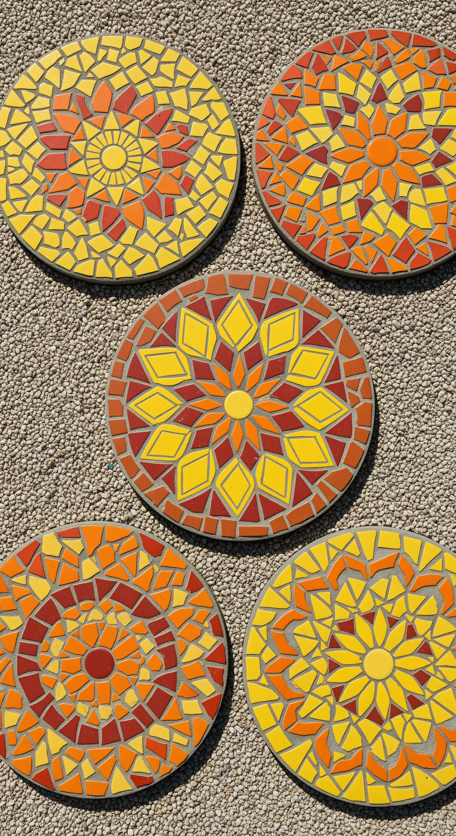 Pietre da giardino rotonde decorate con mosaici a forma di sole nei toni del giallo e arancione.