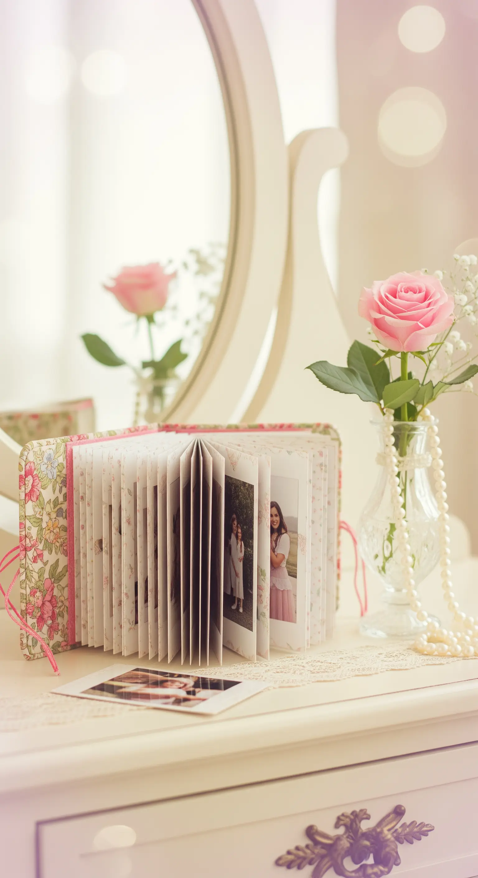 Piccolo album fotografico con copertina in tessuto floreale appoggiato su una toeletta bianca e romantica.