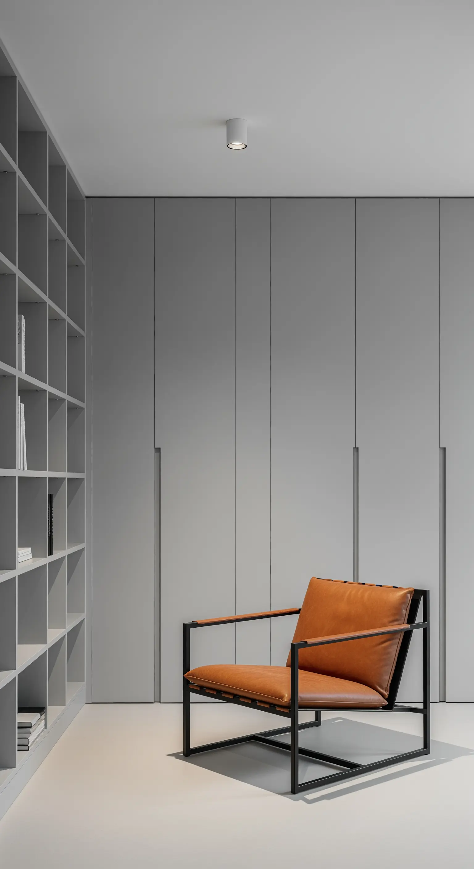 Ambiente minimalista grigio con libreria a muro e poltrona di design in pelle e metallo.