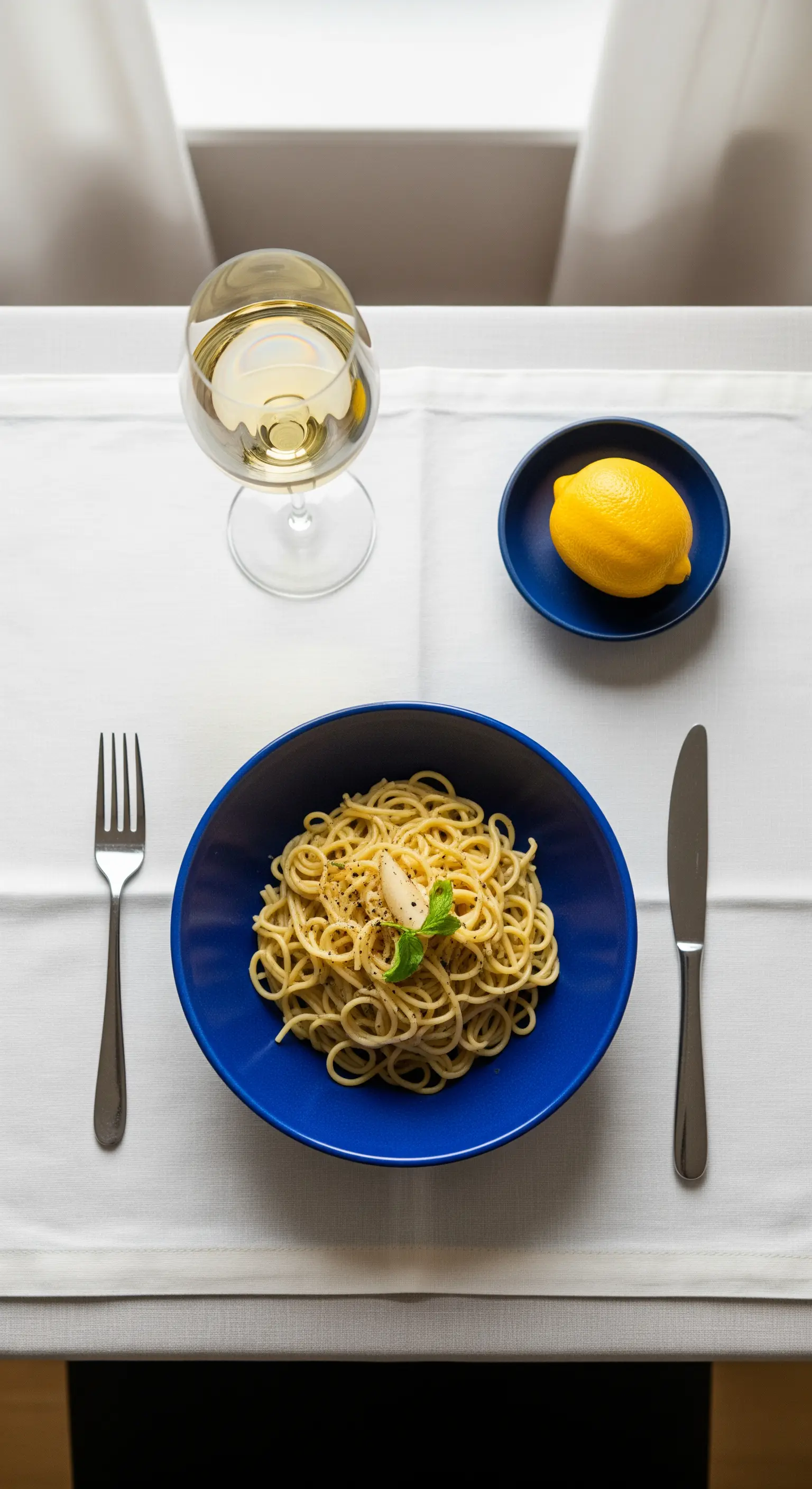 Spaghetti al limone in una ciotola blu profondo, con un limone a fianco.