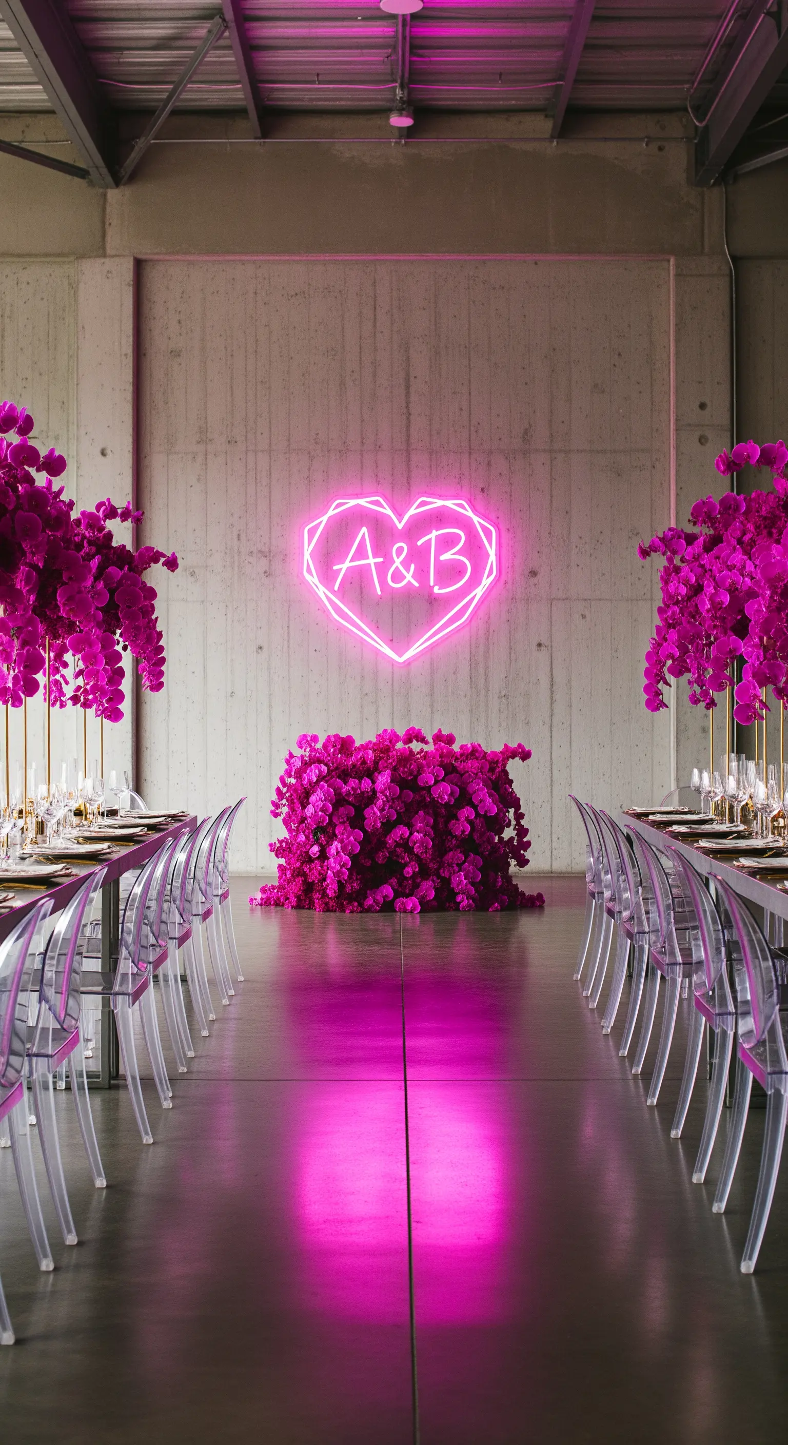 Cuore al neon fucsia con iniziali in una sala di cemento, con fiori dello stesso colore.
