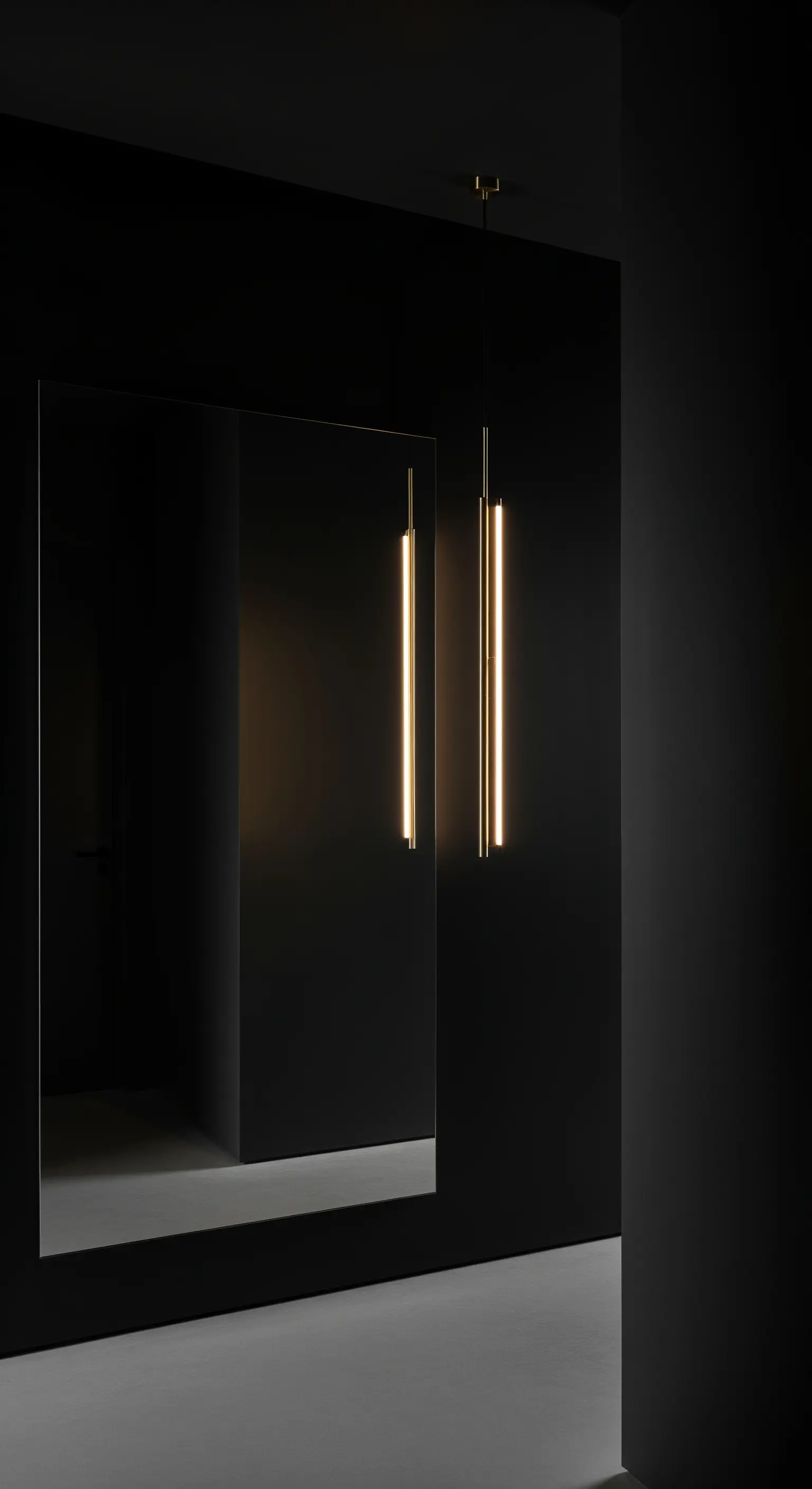 Spazio completamente nero con un grande specchio senza cornice e due lampade lineari in ottone.