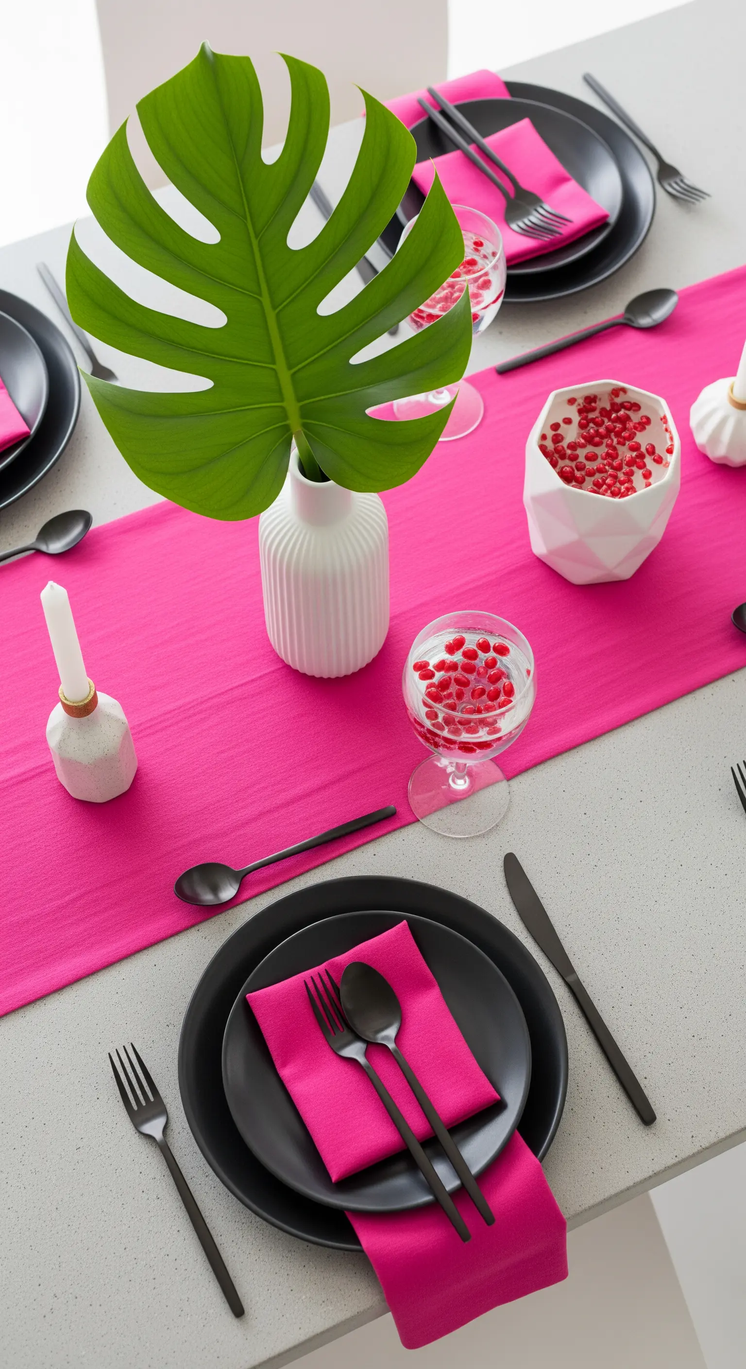 Tavola minimalista con runner fucsia, stoviglie nere e una foglia di Monstera.