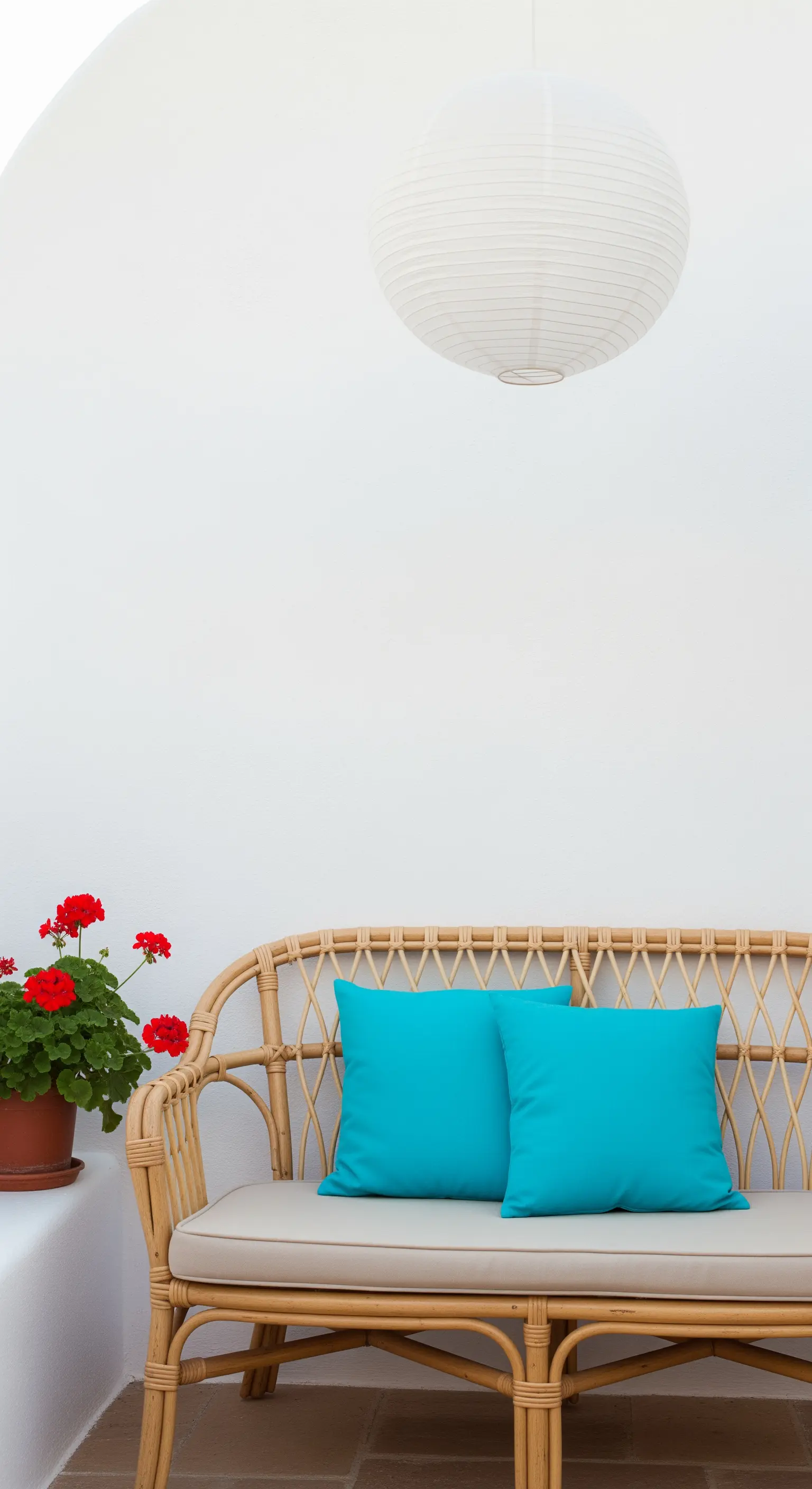 Divanetto in rattan con due cuscini turchesi contro una parete bianca, con lanterna di carta.