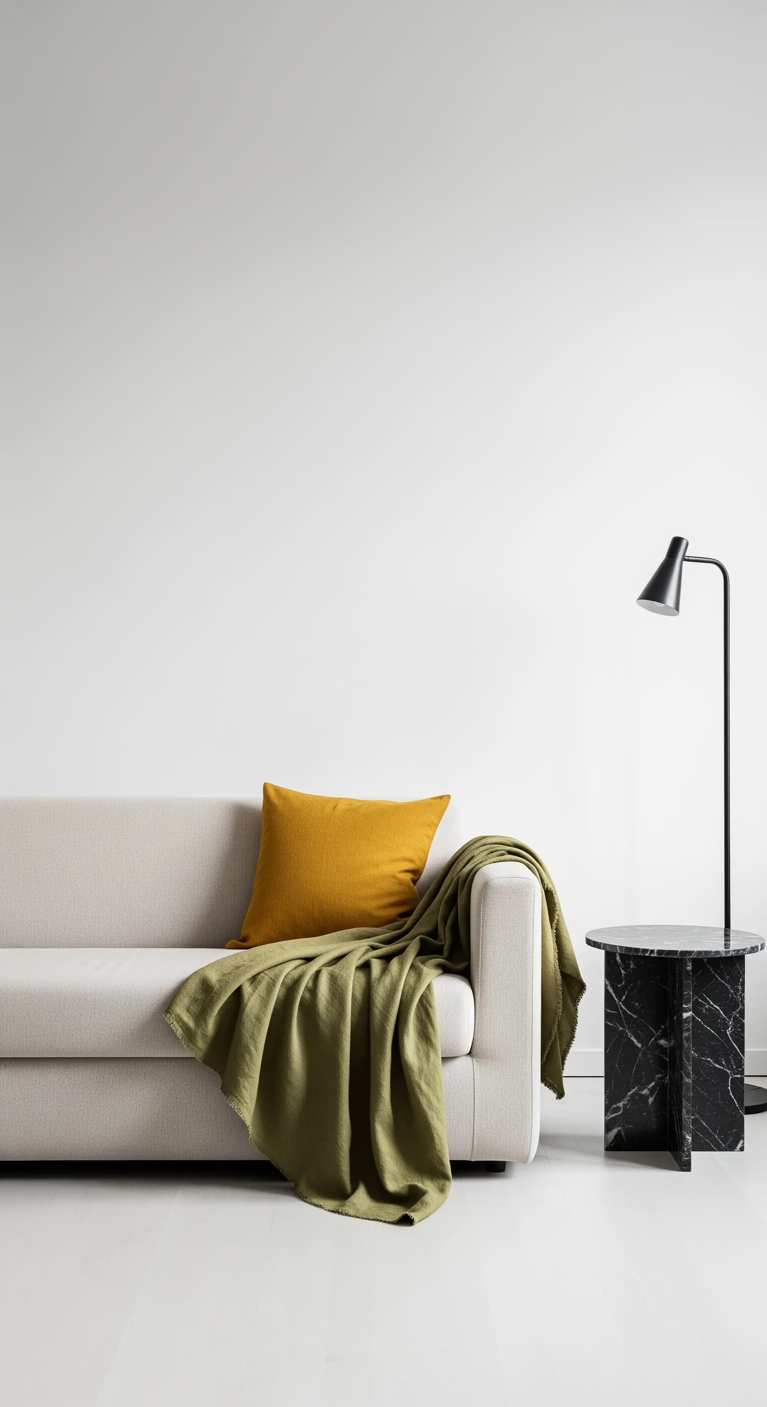 Dettaglio di un divano minimalista con cuscino senape, coperta verde e tavolino in marmo nero.