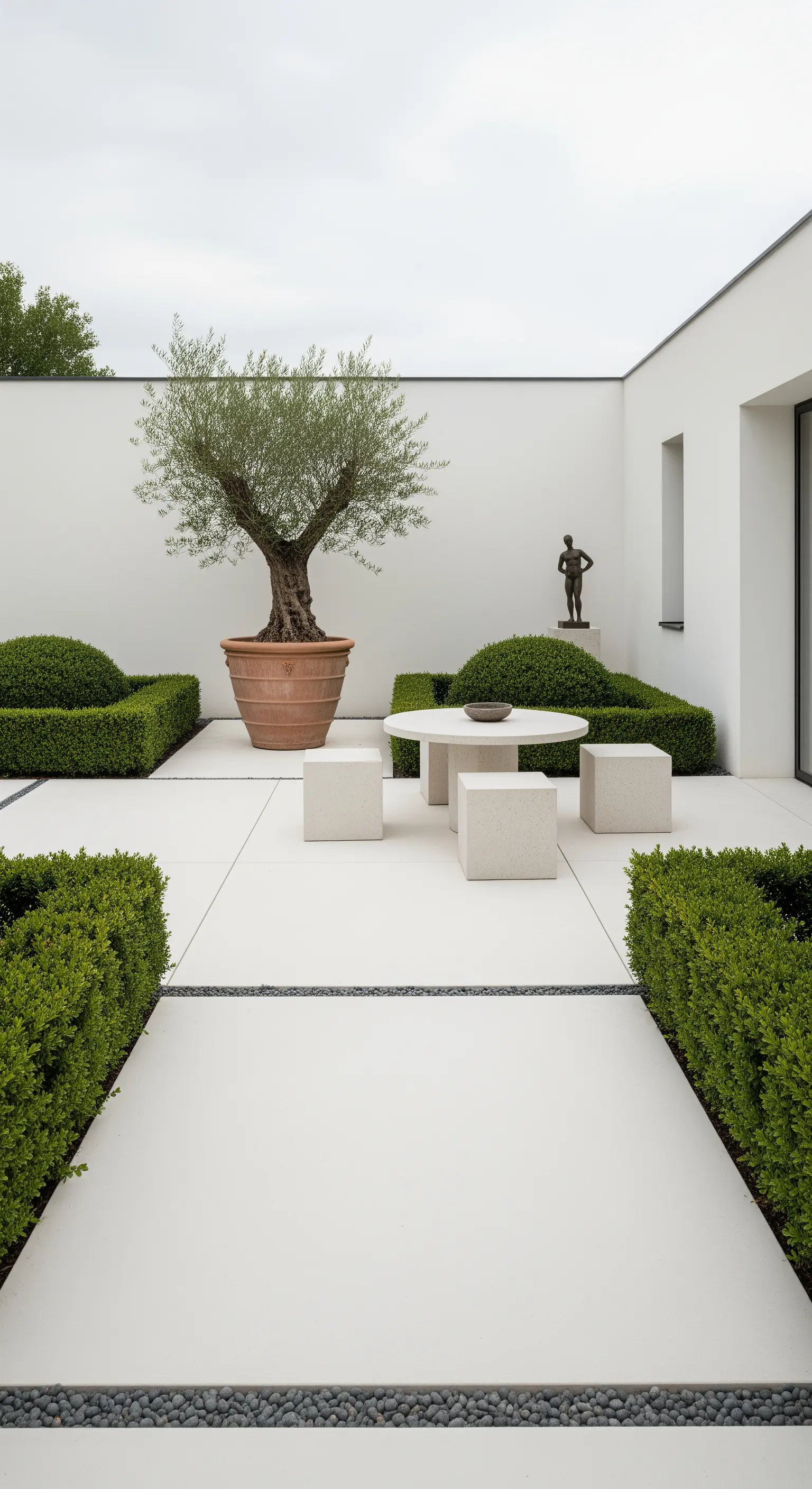 Patio minimalista con ulivo in vaso, siepi basse e sedute a cubo in pietra chiara.
