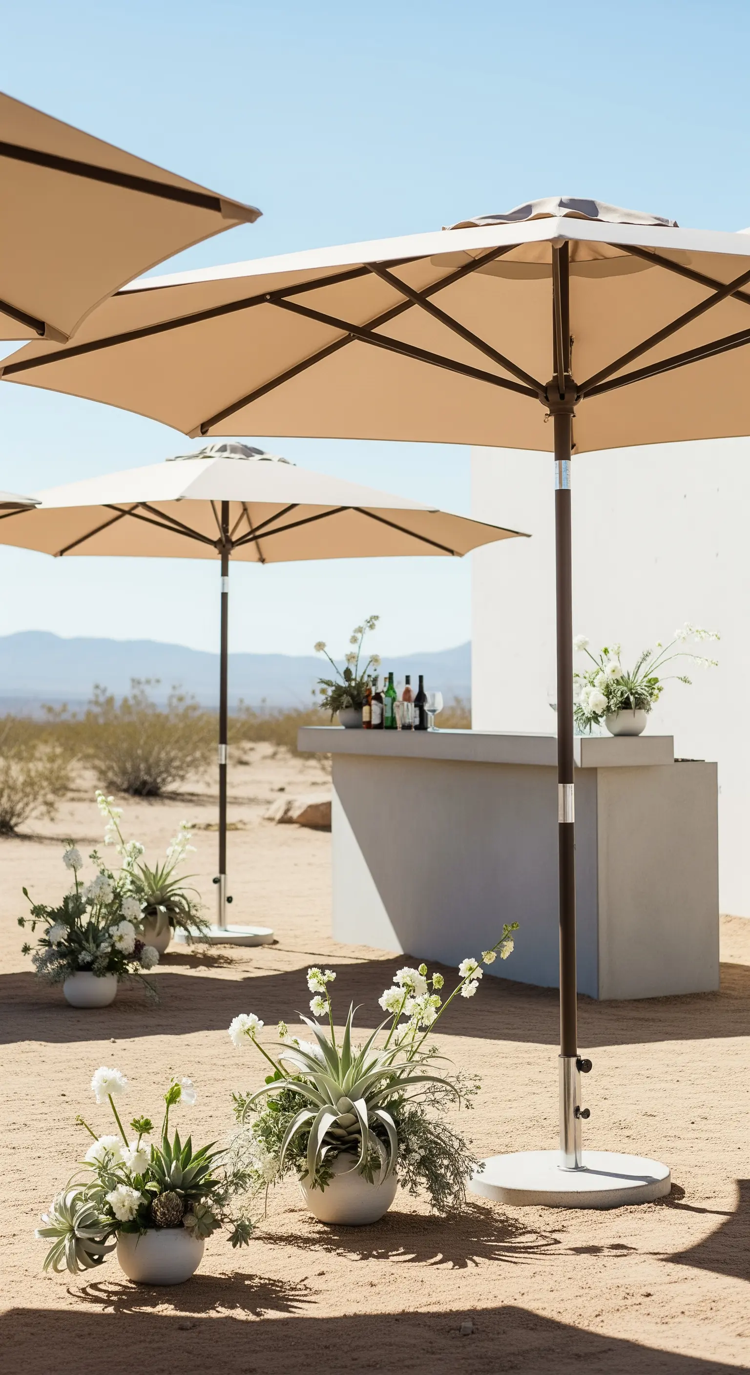 Allestimento minimalista nel deserto con bar in cemento, ombrelloni beige e piante grasse