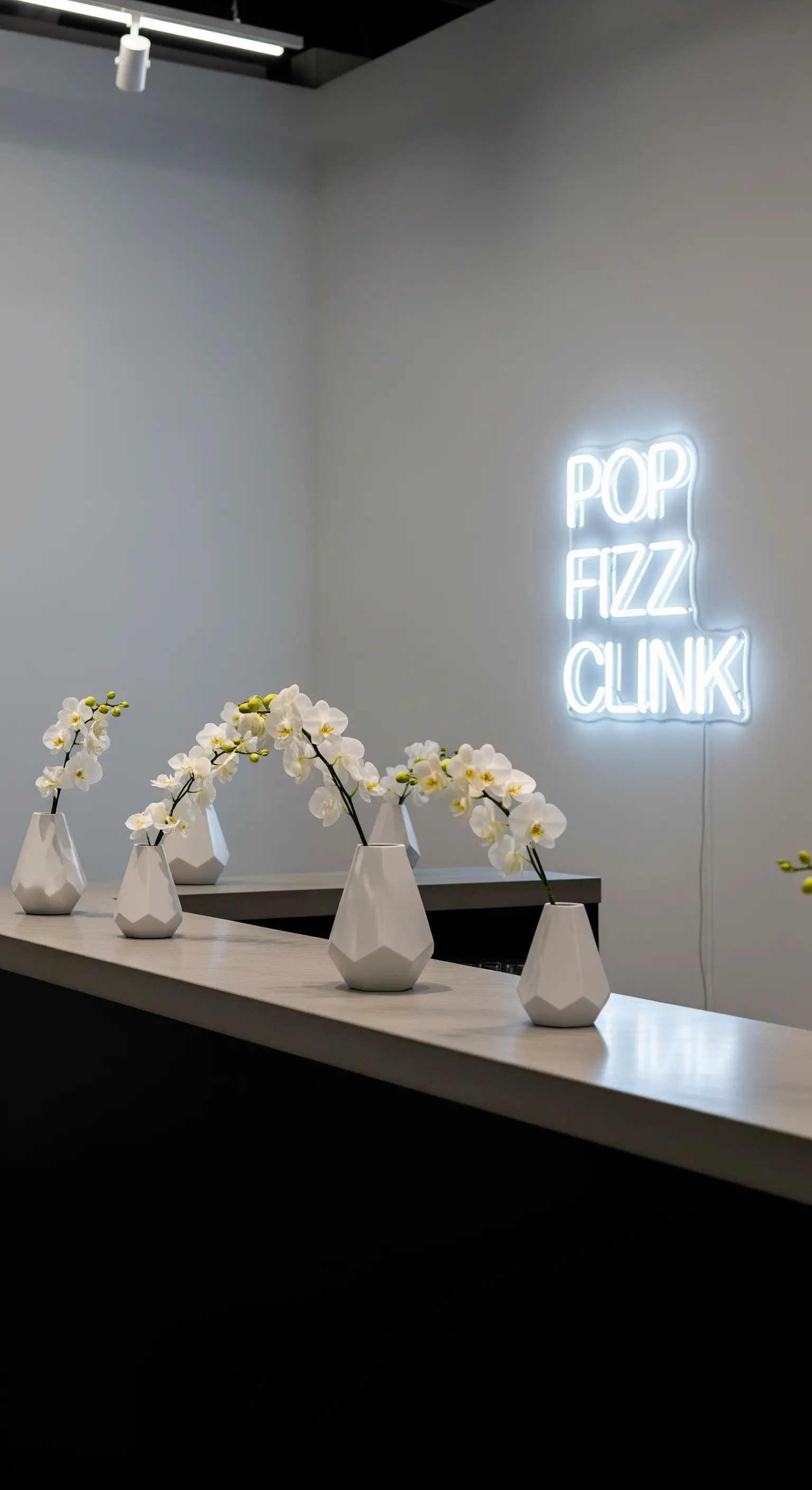 Bancone bar minimalista con insegna al neon bianca e vasi geometrici con orchidee bianche.
