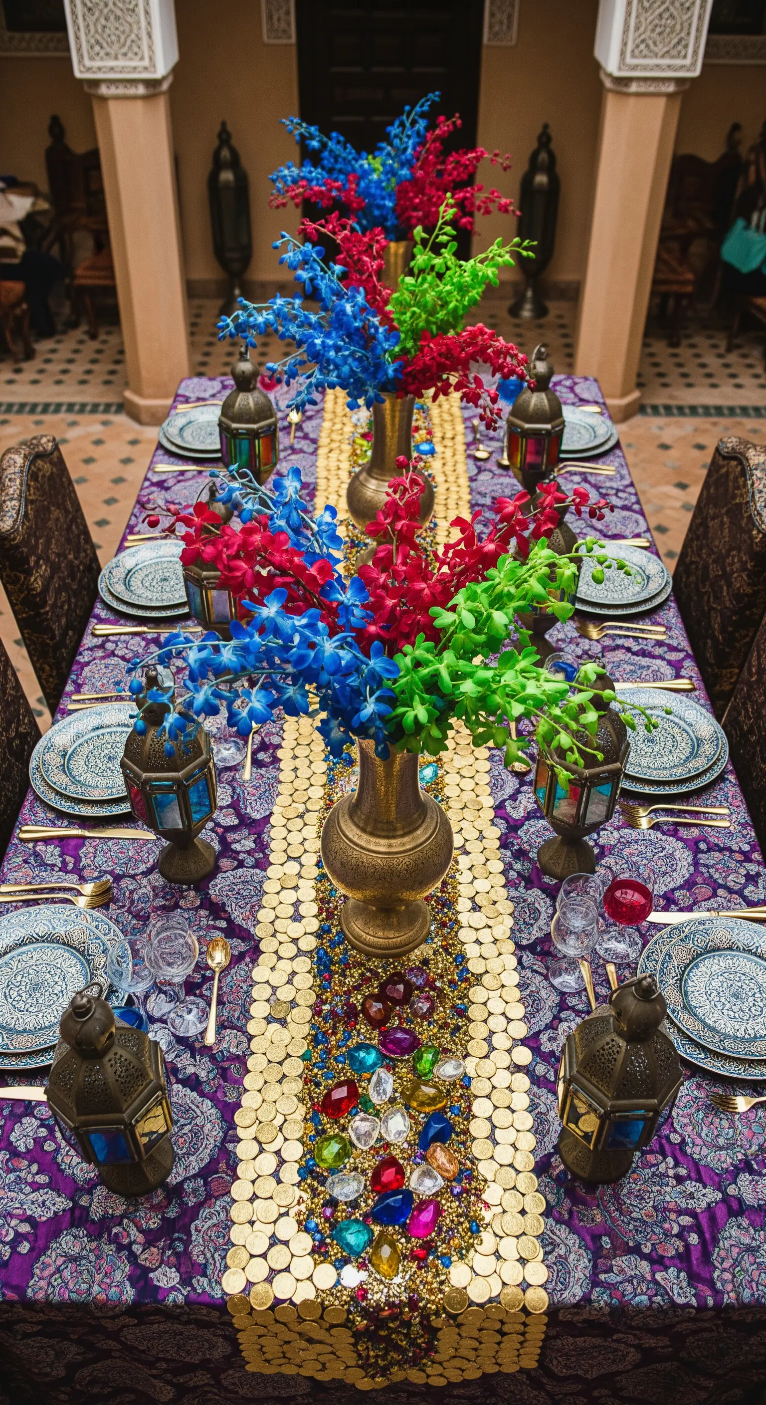 Tavolo in stile marocchino con runner di gemme e monete, e orchidee dai colori primari.