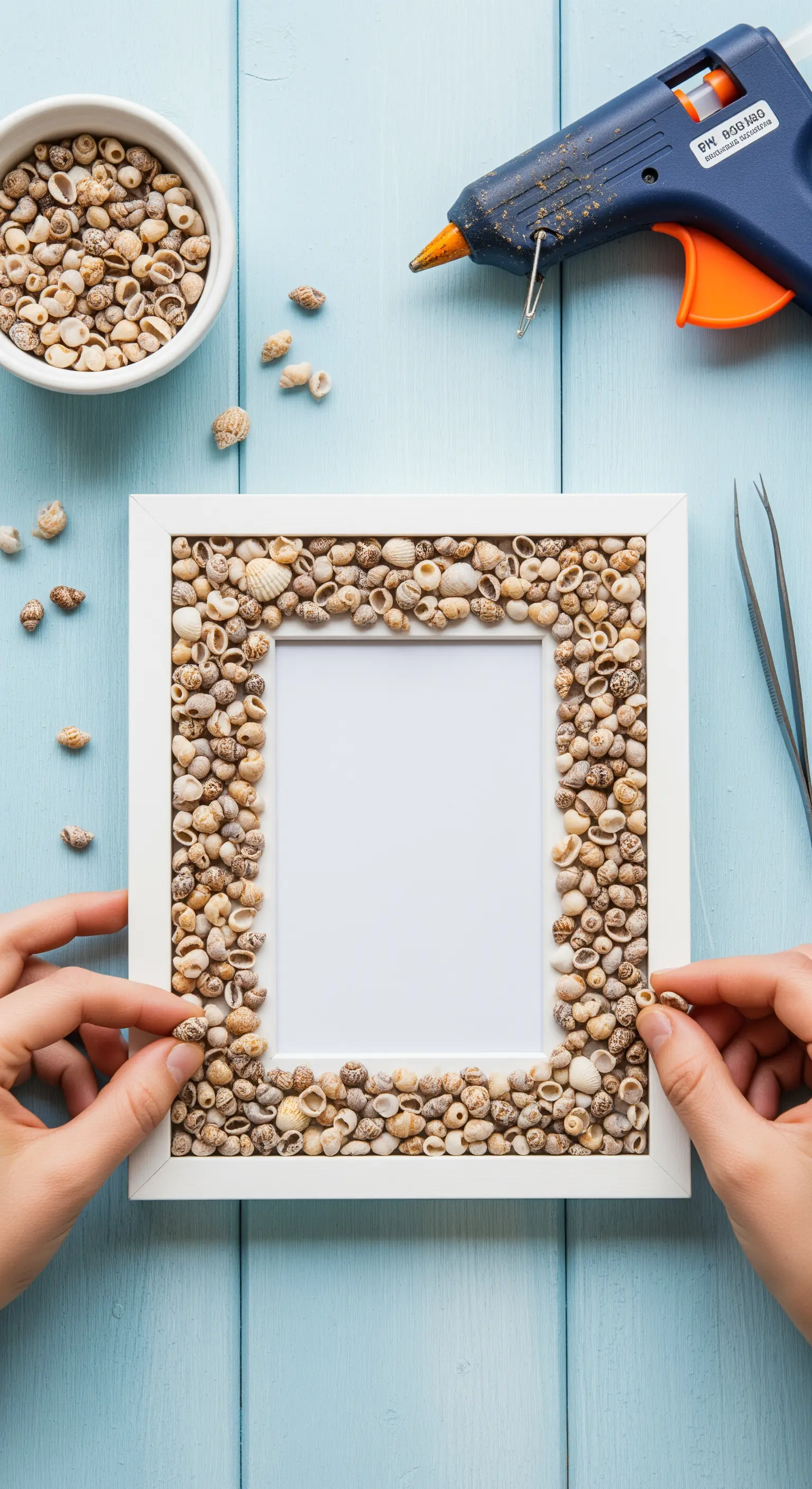 Mani che applicano piccole conchiglie su una cornice bianca con una pistola per colla a caldo.