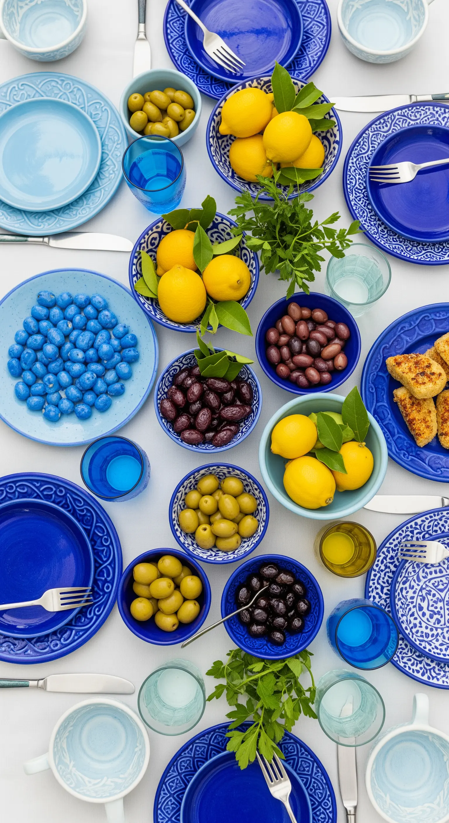 Tavola imbandita con un mix di ciotole e piatti blu, olive e limoni.