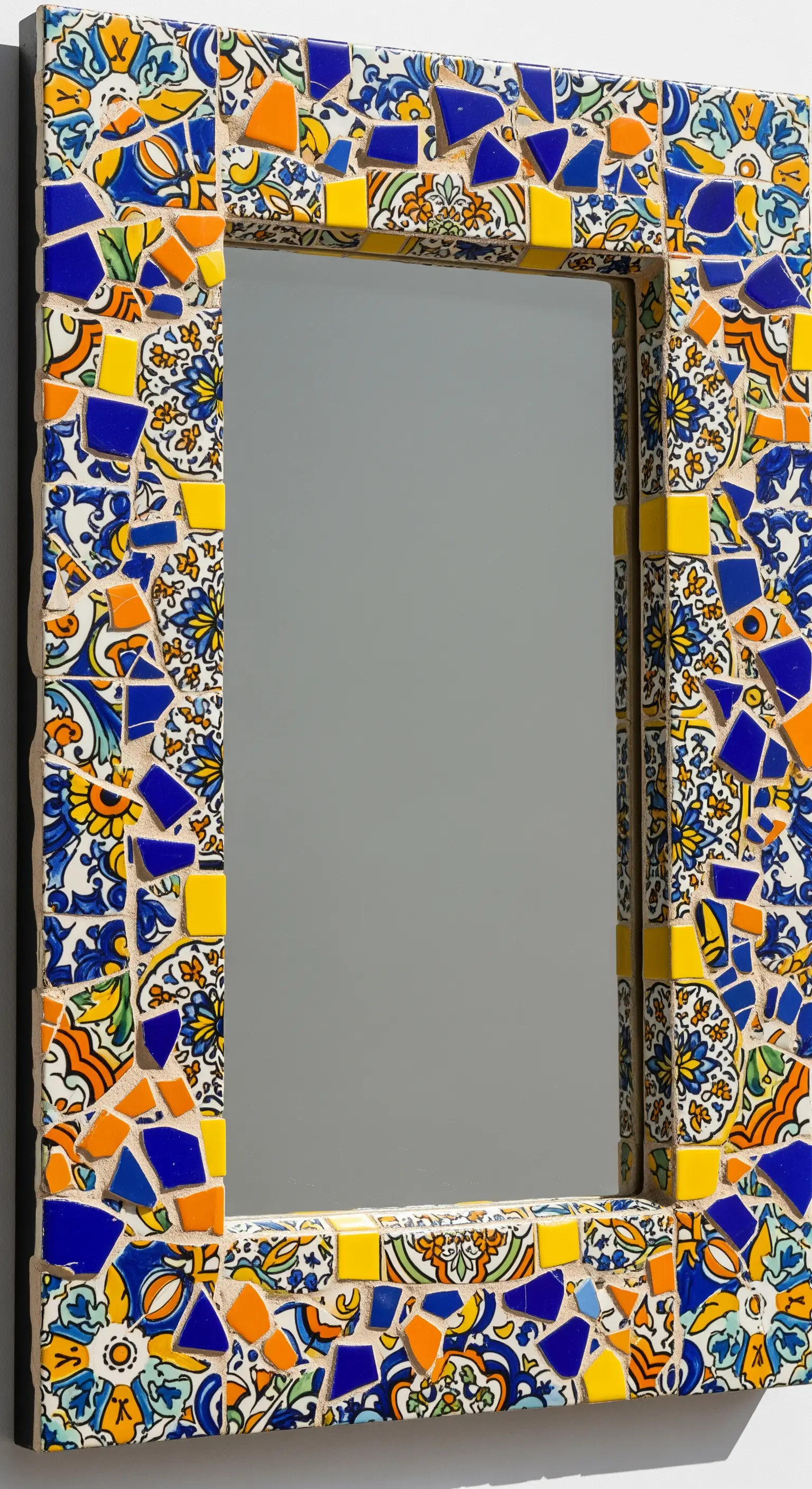 Dettaglio di una cornice per specchio realizzata con un mosaico di piastrelle rotte colorate.