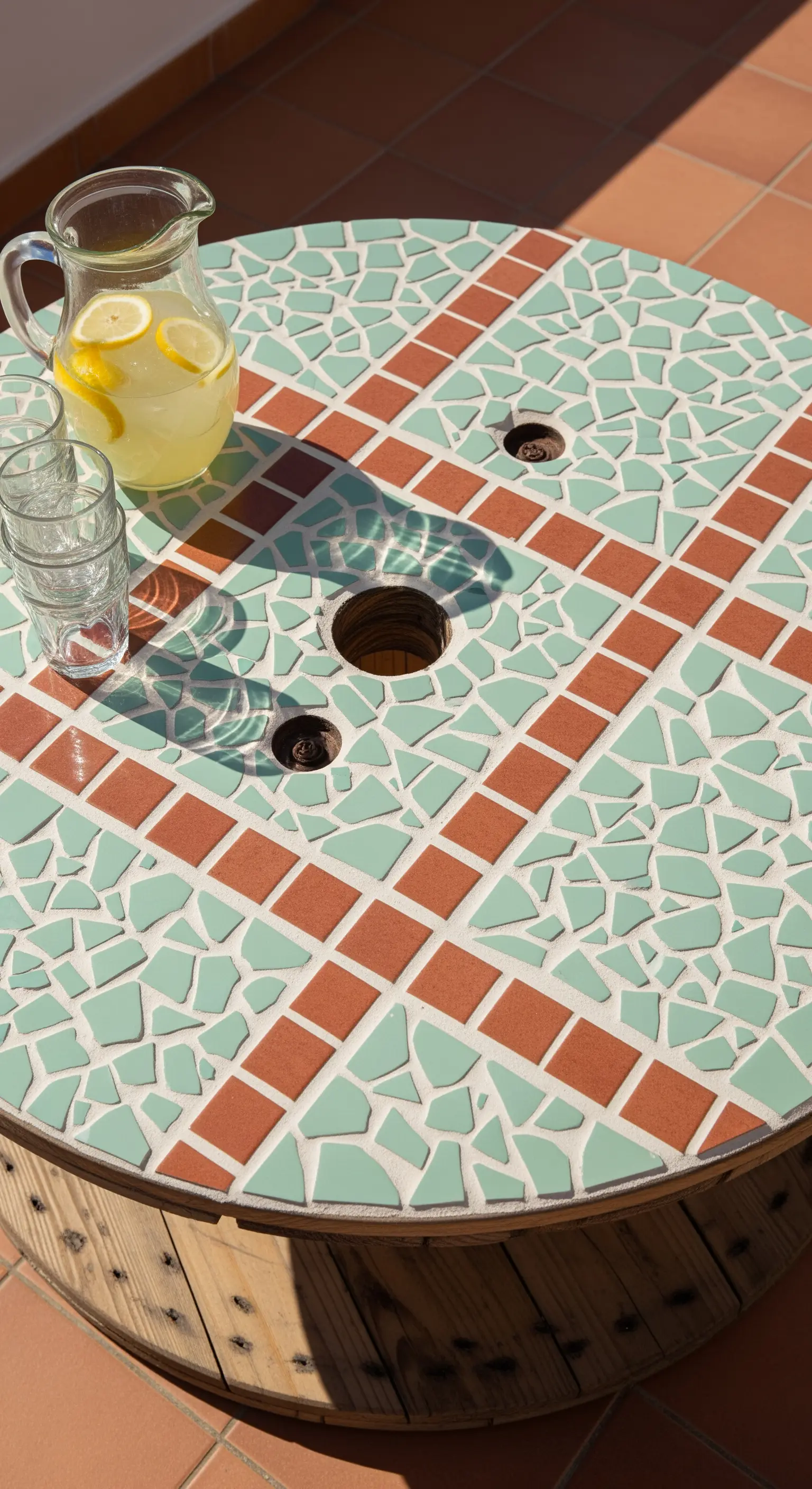 Piano di un tavolino a bobina decorato con un mosaico di piastrelle verdi e terracotta.