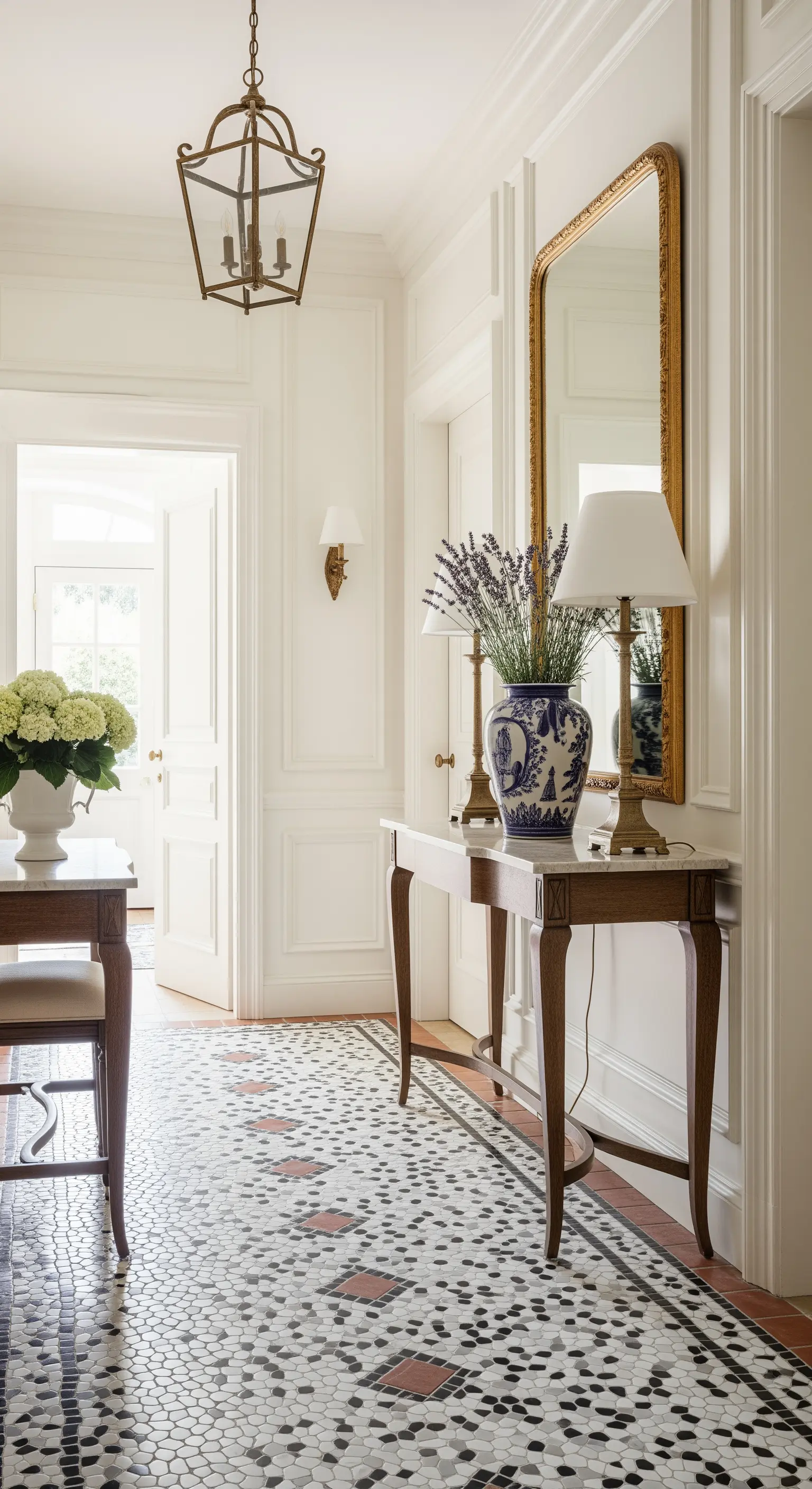 Ingresso elegante con pavimento a mosaico, boiserie bianca e consolle con specchio dorato.