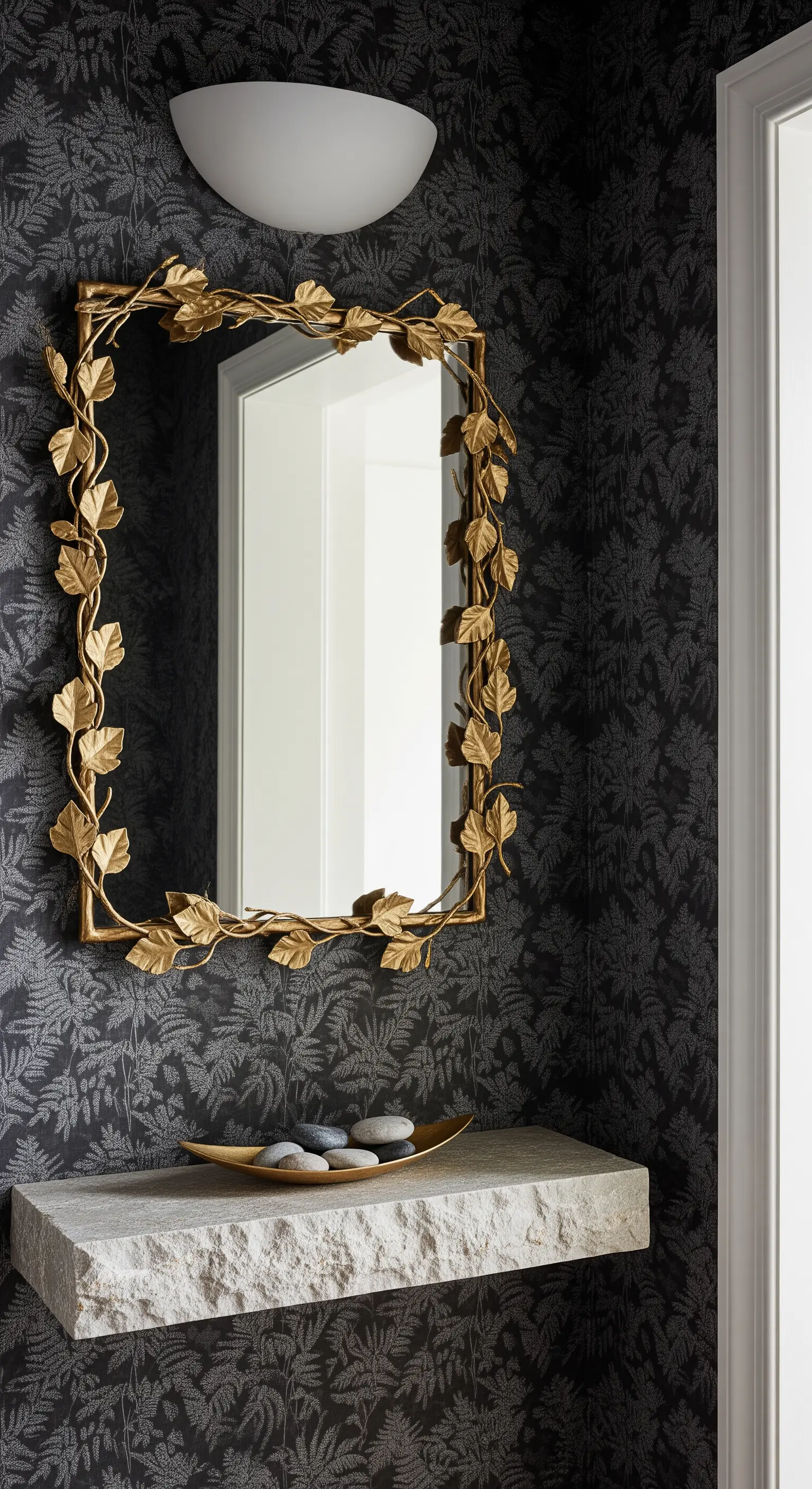 Carta da parati antracite a motivi di foglie con mensola in pietra e specchio dorato a forma di rami.
