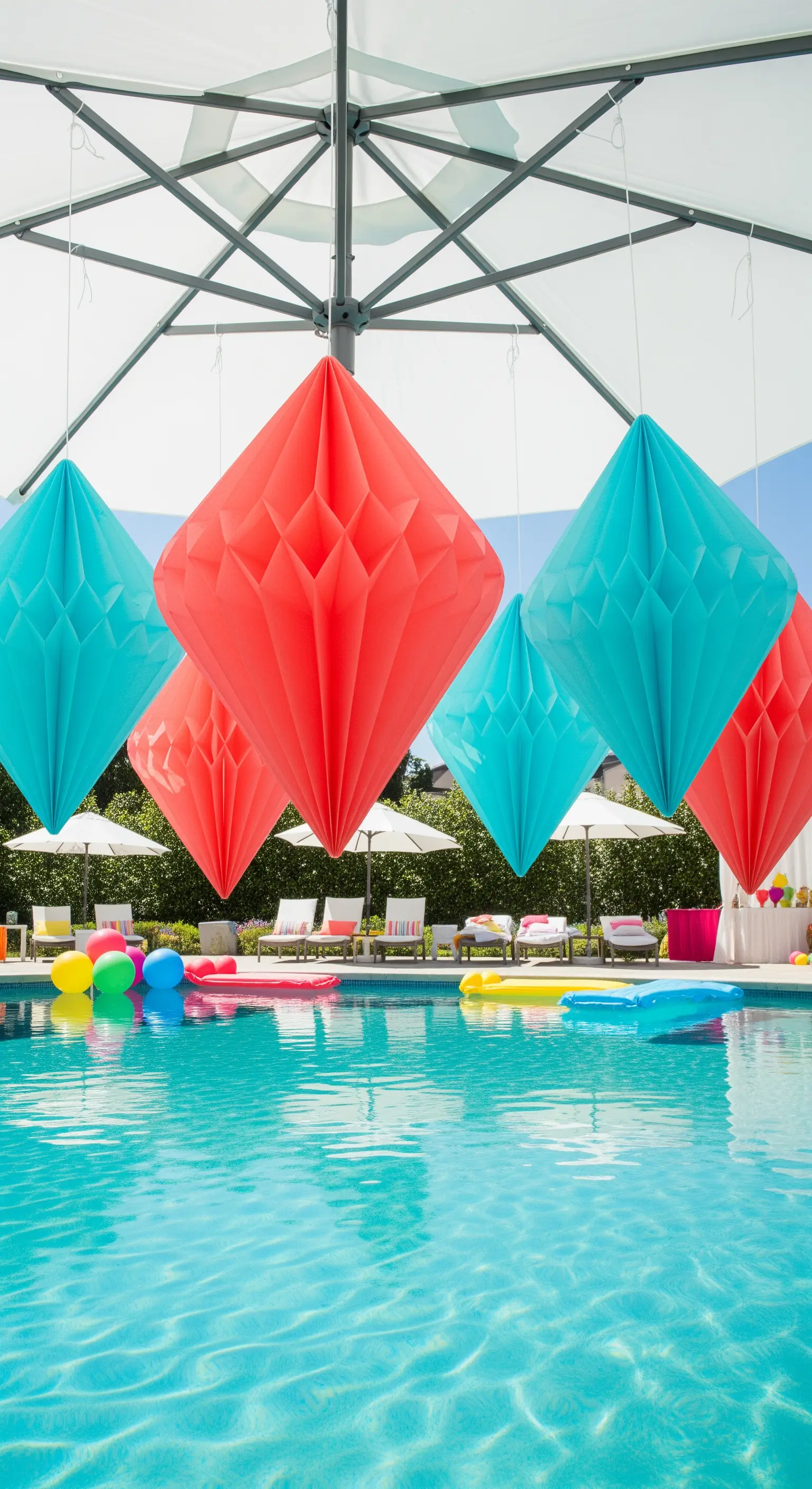 Decorazioni di carta a nido d'ape a forma di diamante, rosse e turchesi, sospese sopra una piscina.