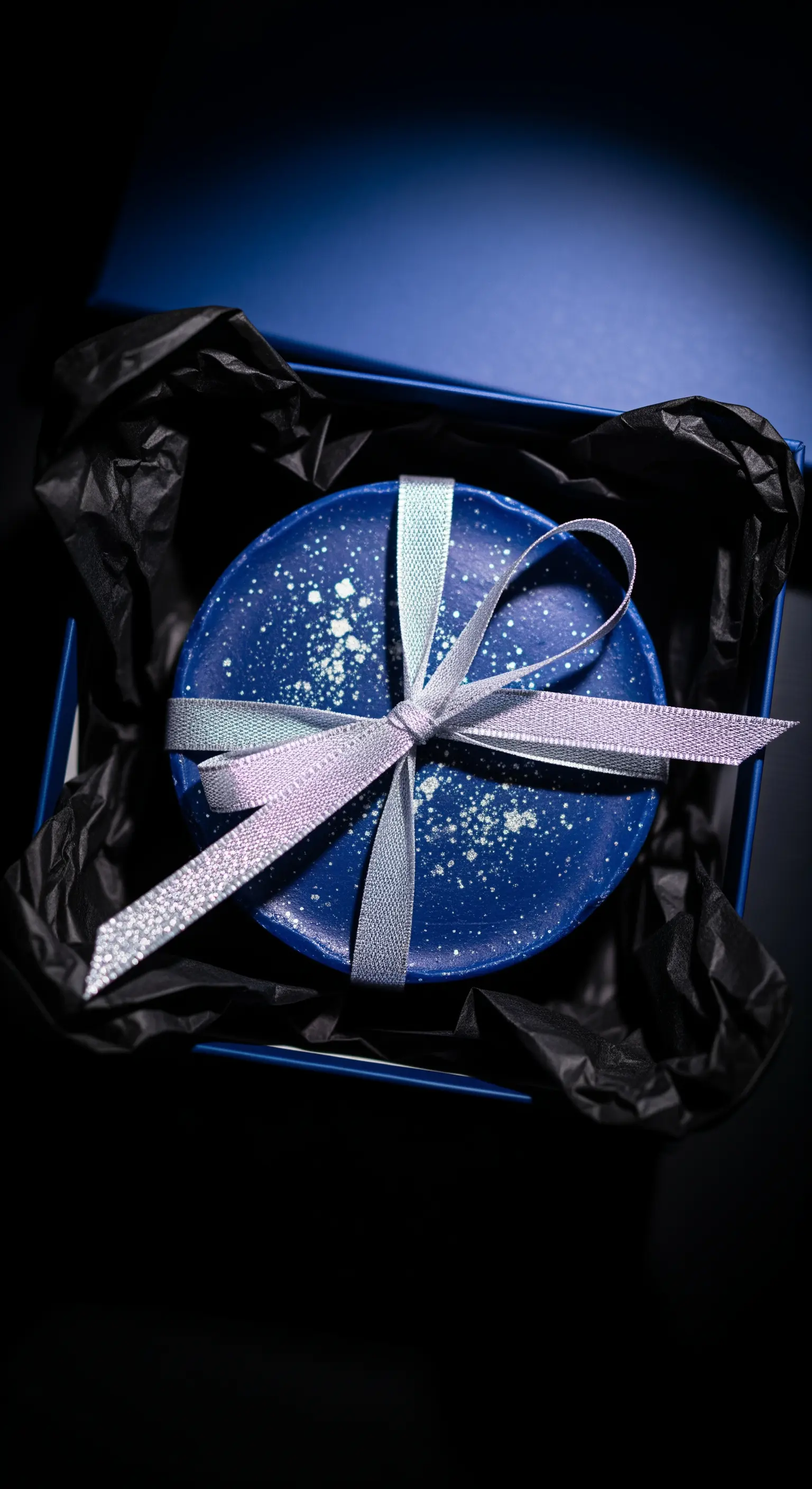 Sapone blu scuro con schizzi bianchi in una scatola blu, con un fiocco argentato glitterato.