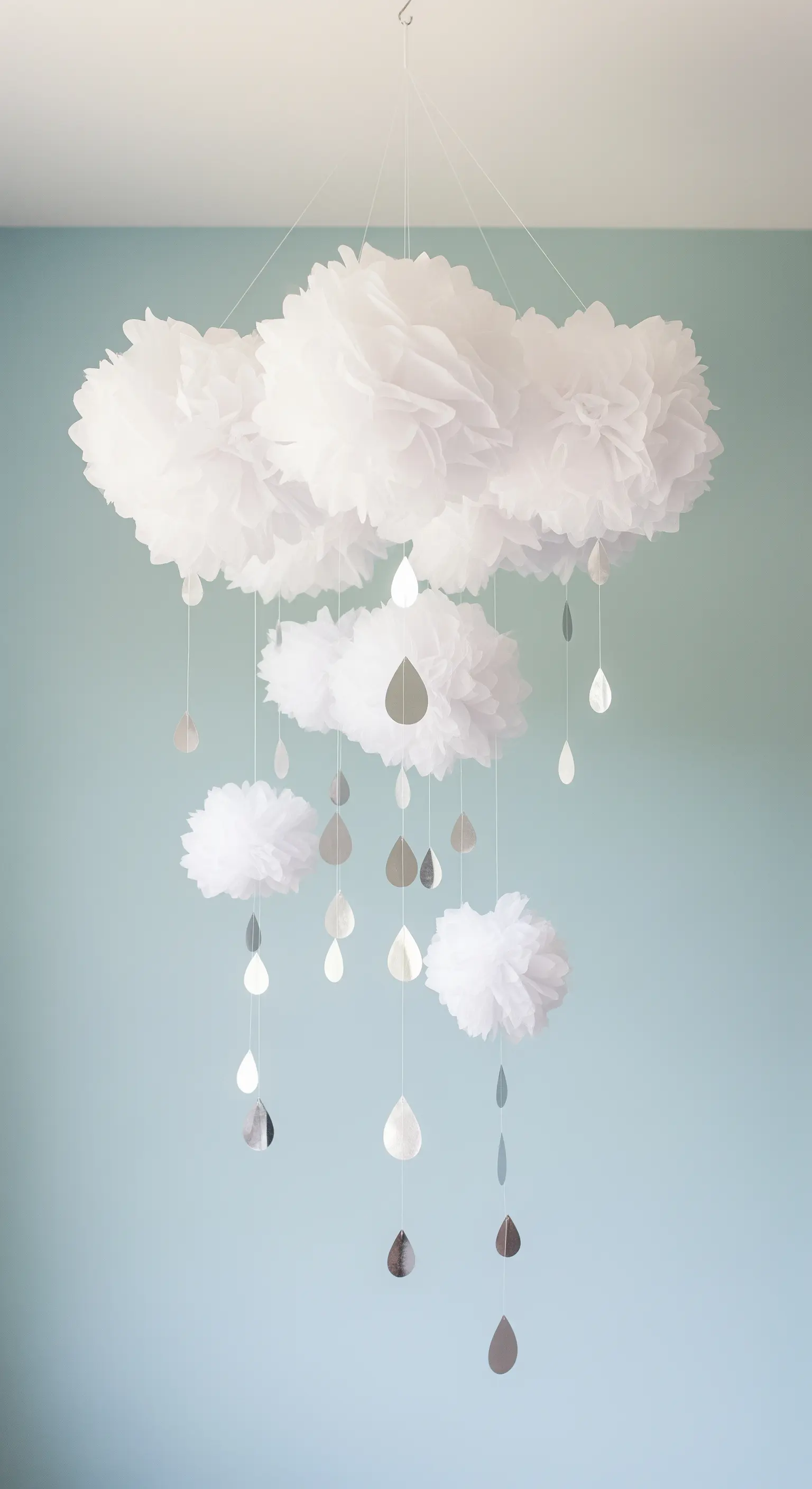 Giostrina sospesa con nuvole di pompon di carta velina bianca e gocce di pioggia argentate.