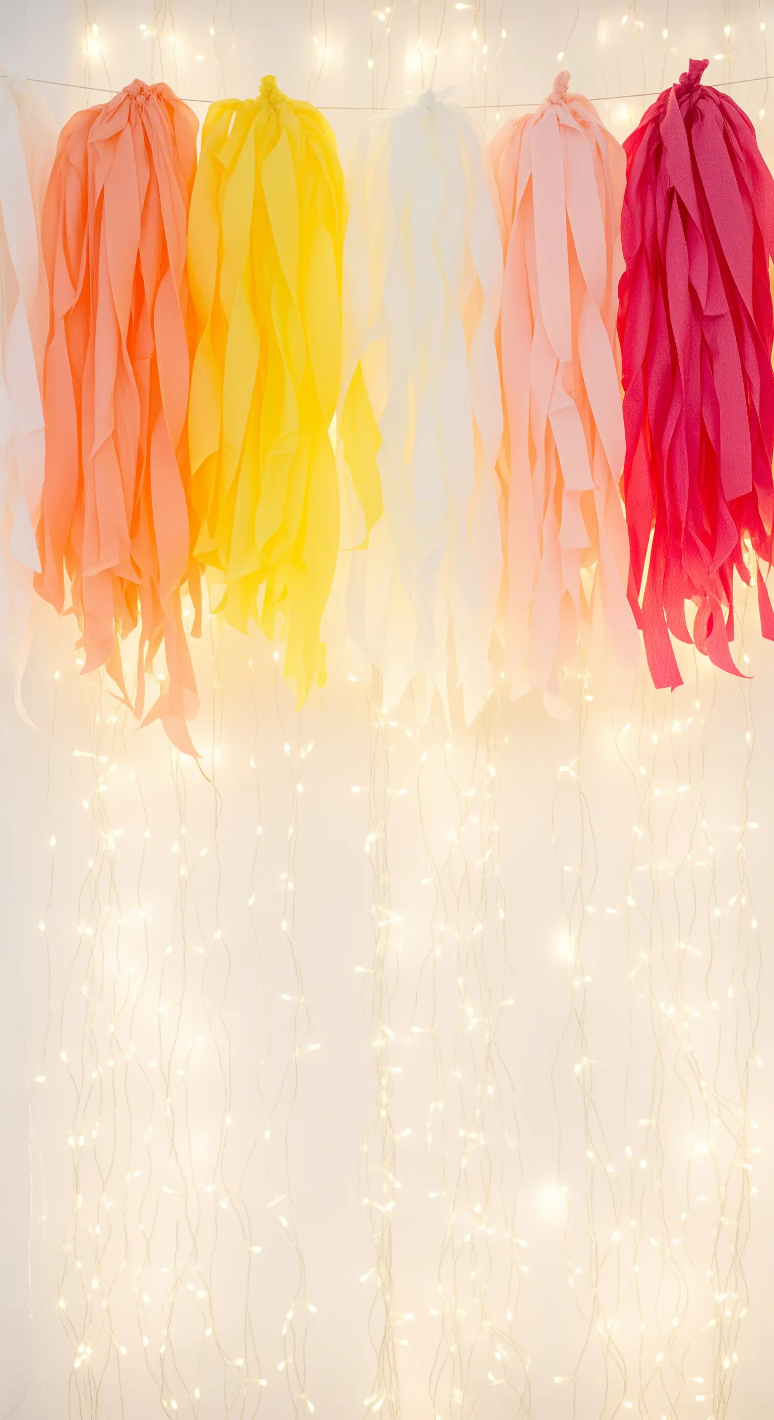 Nappe di carta colorata sospese sopra una parete interamente coperta da lucine calde.