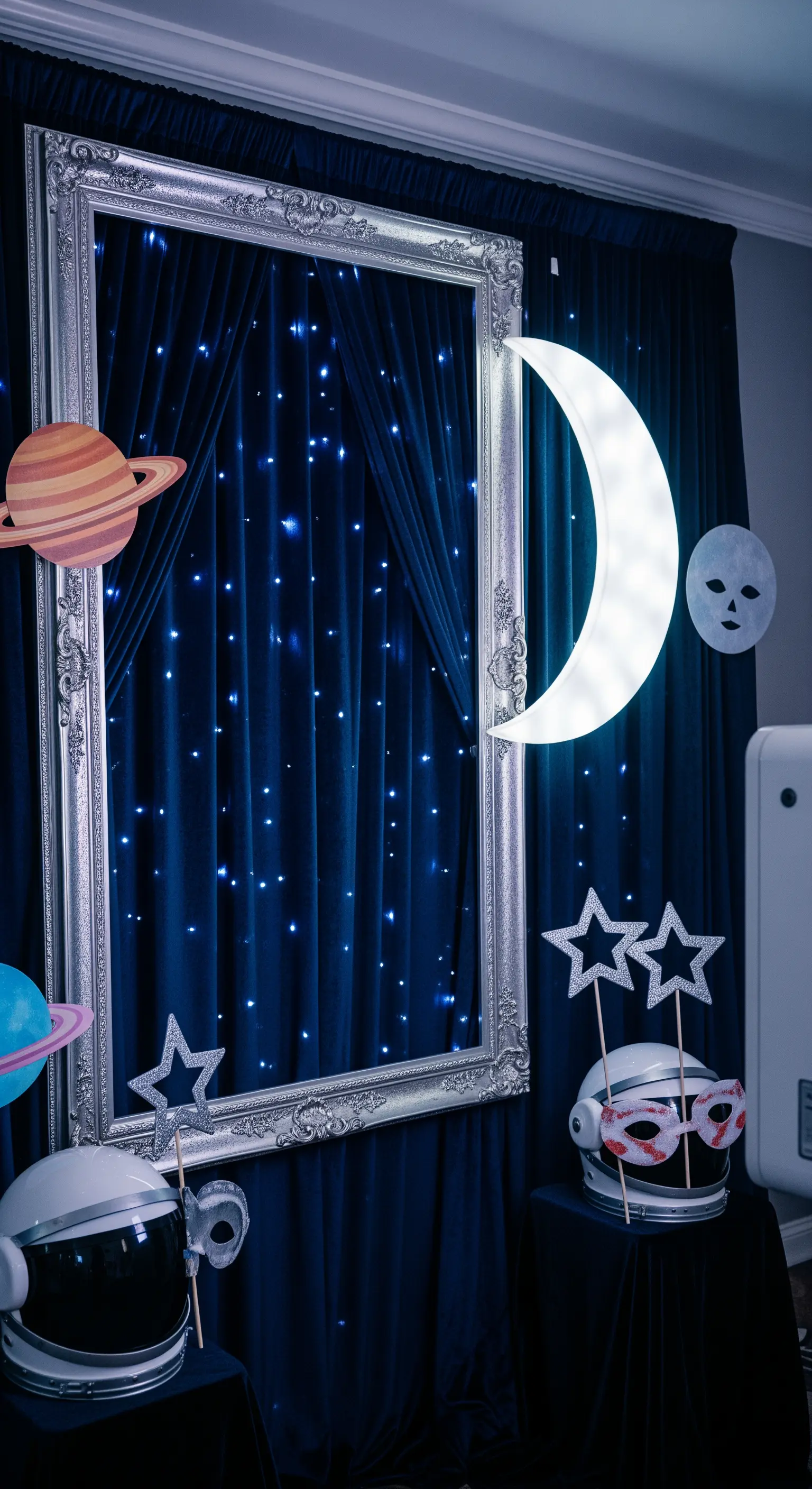 Photo booth a tema spaziale con sfondo stellato, luna luminosa e caschi da astronauta come accessori.