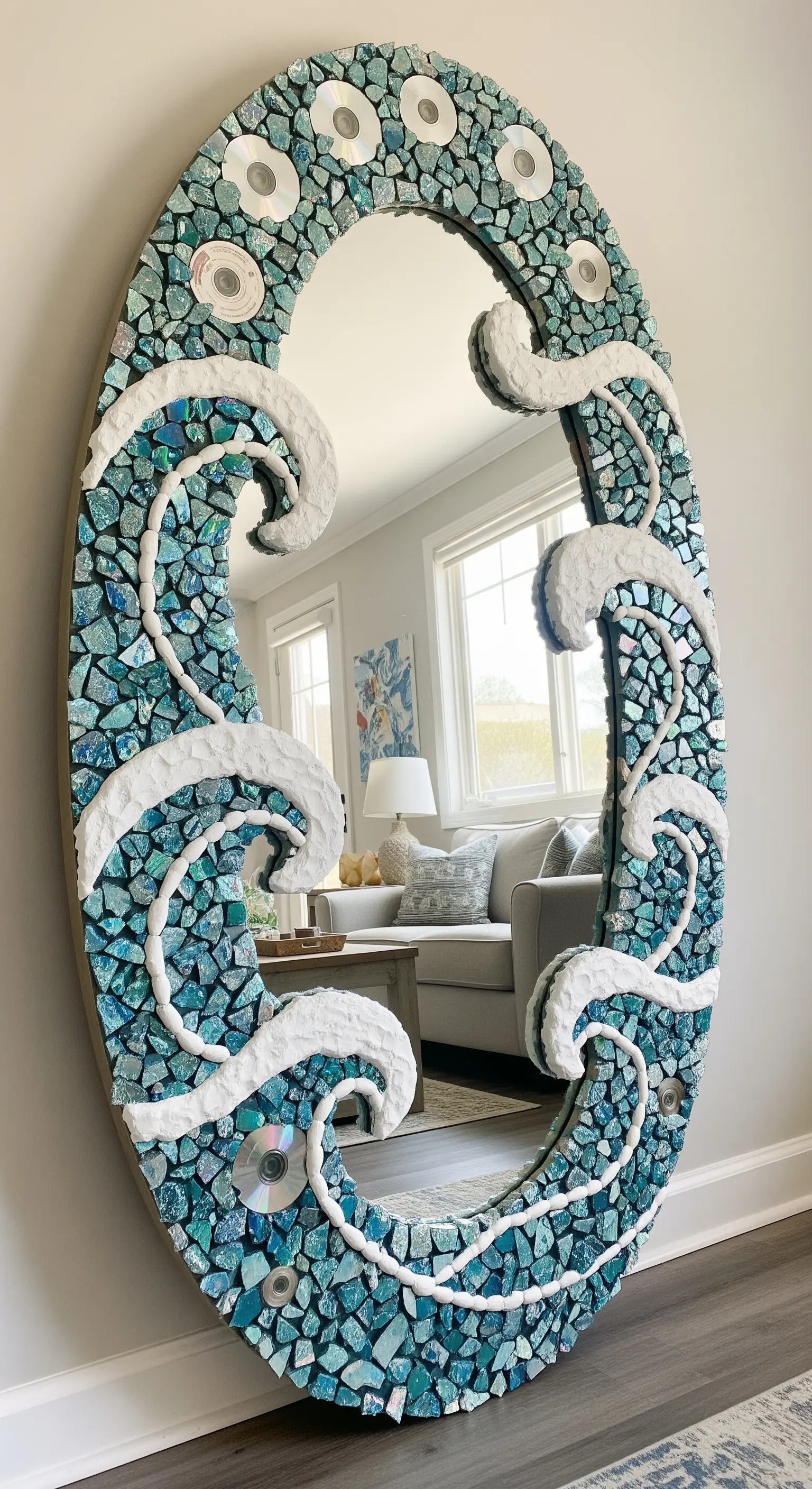 Specchio ovale con una cornice a mosaico che imita le onde del mare, con dettagli bianchi in rilievo.
