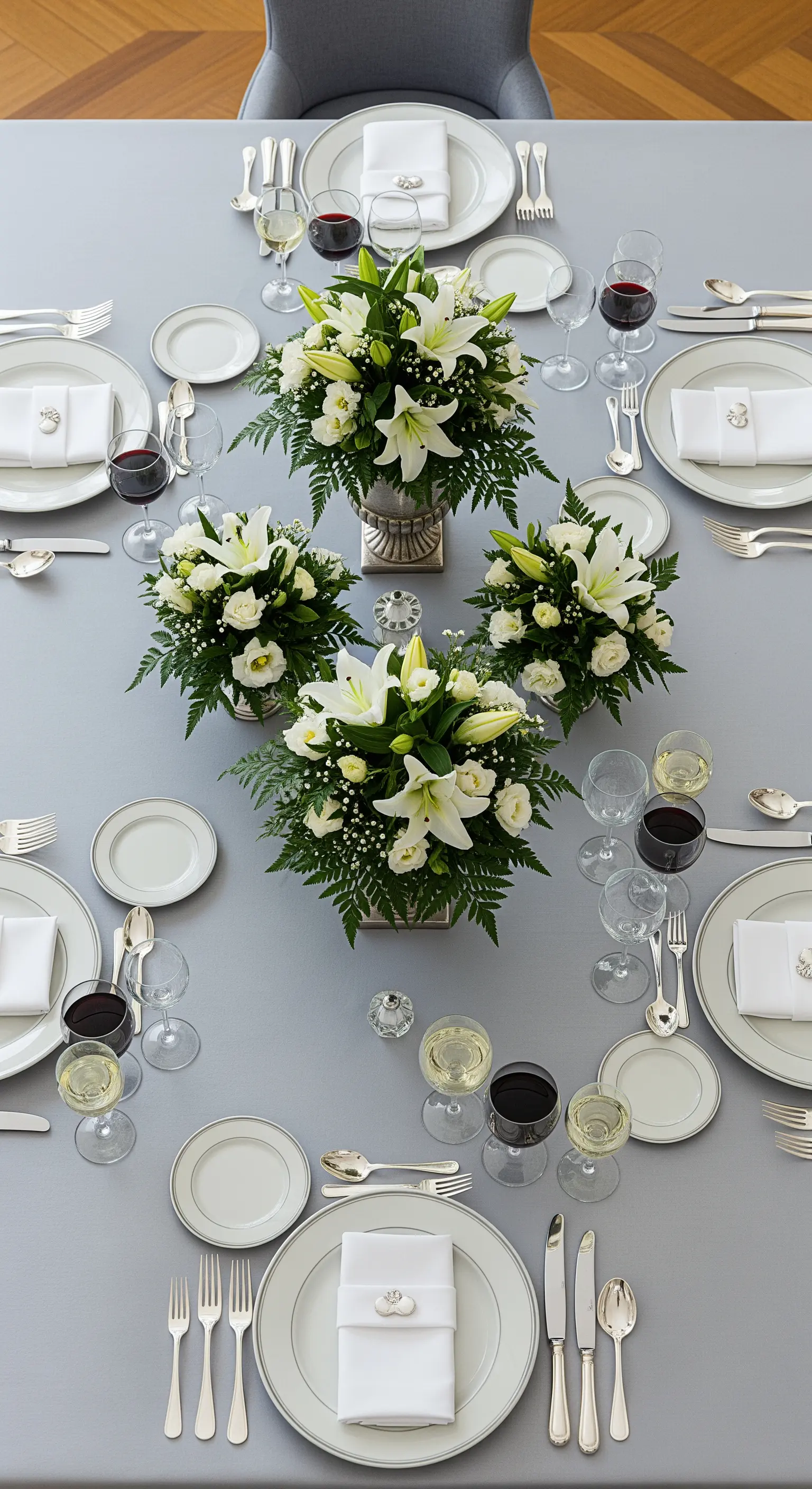 Tavola formale con tovaglia grigio perla e quattro centrotavola simmetrici di gigli bianchi.