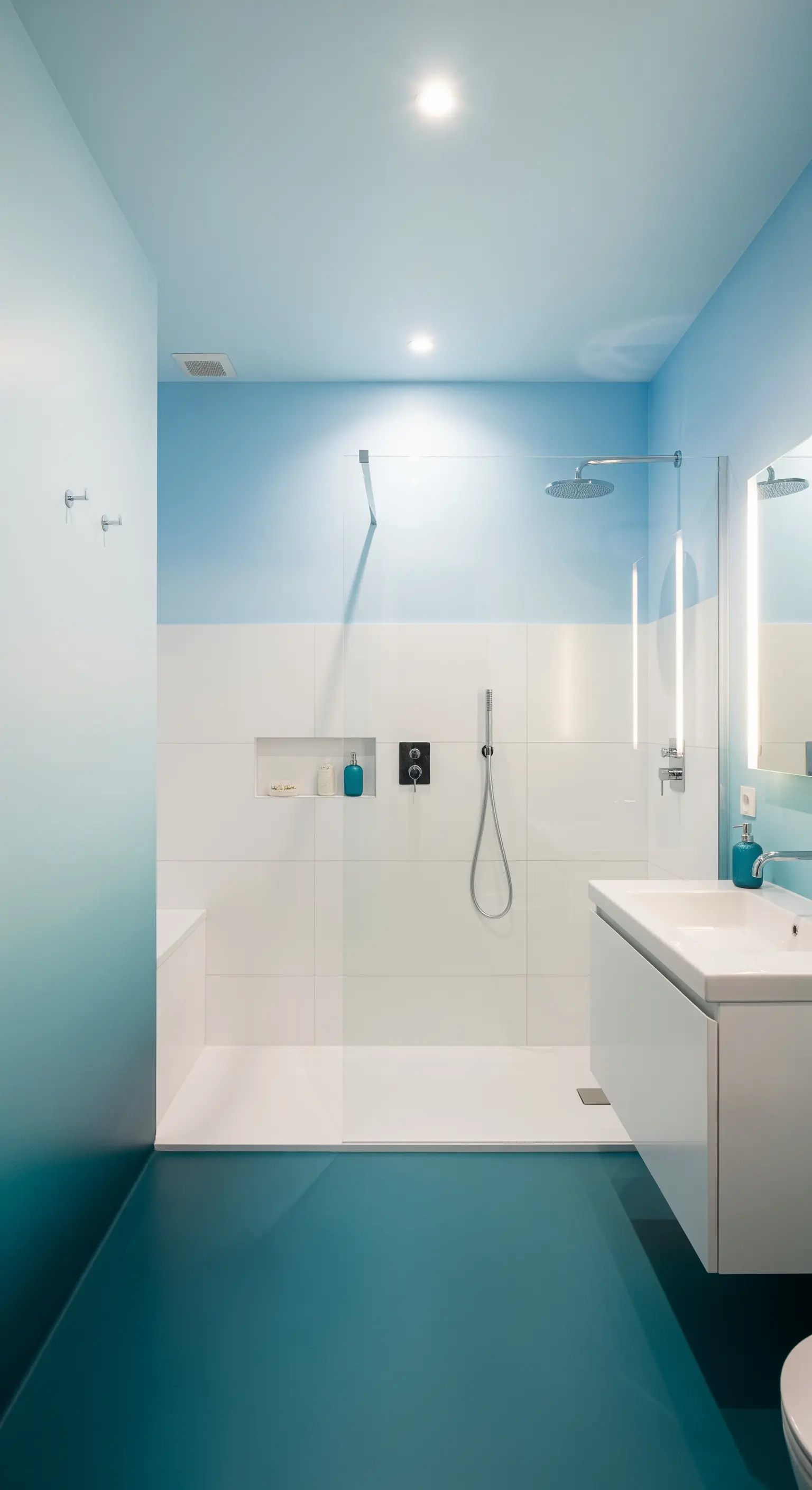 Bagno minimalista con pareti e pavimento sfumati dal turchese al bianco e arredi bianchi.