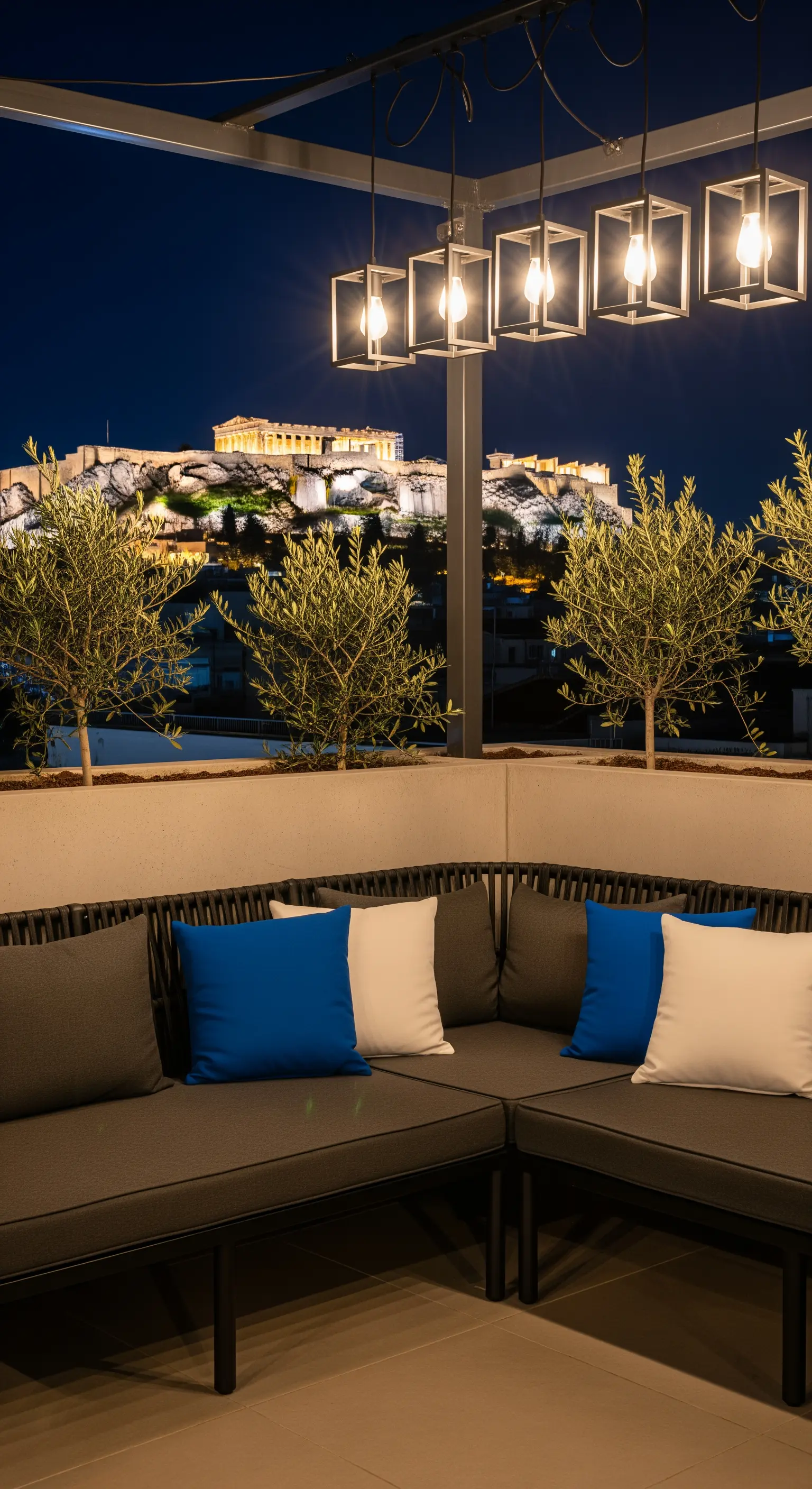 Terrazza moderna con vista sull'Acropoli, divano grigio e lampade cubiche sospese.
