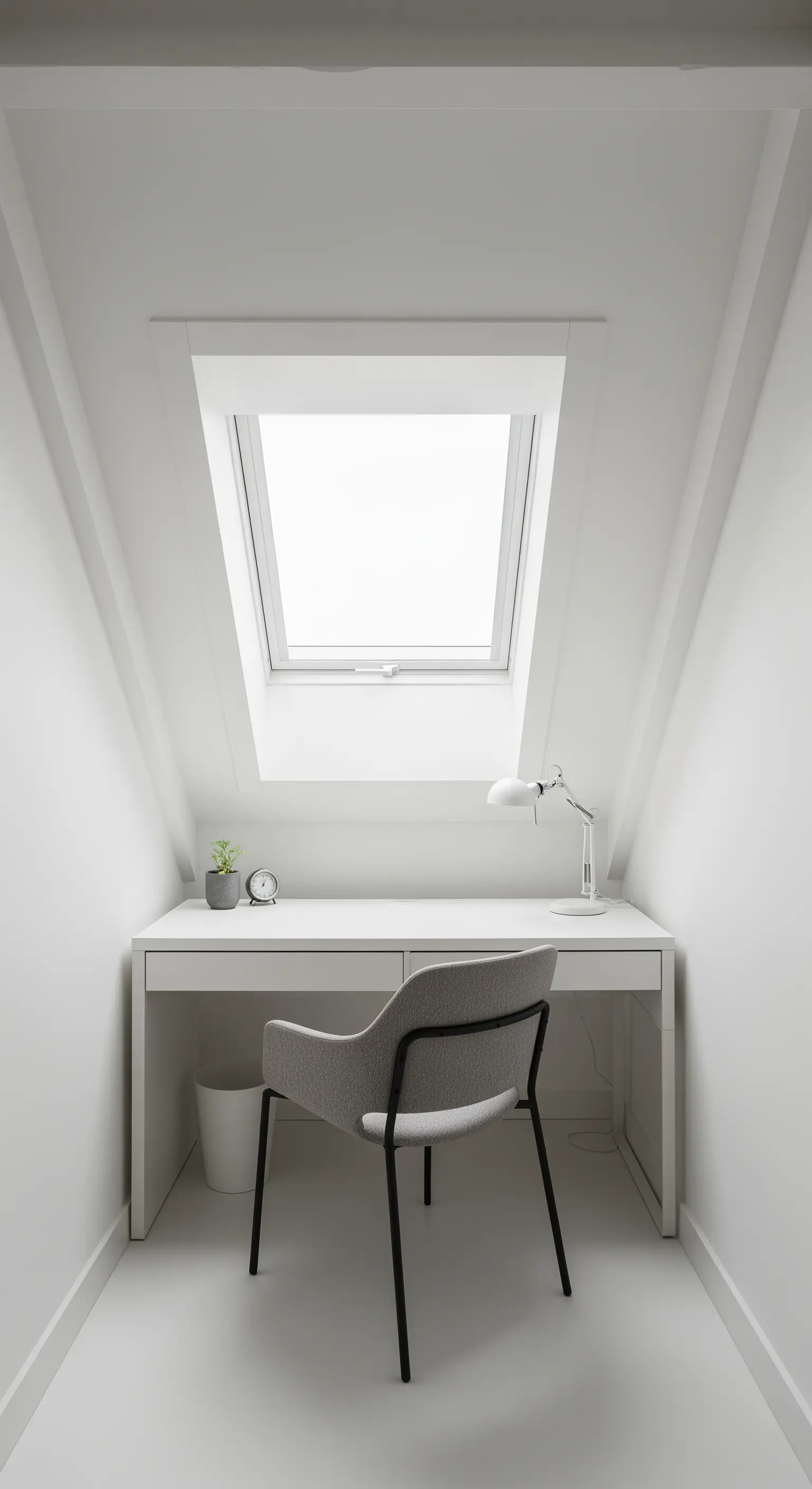 Piccolo home office bianco ricavato in una mansarda sotto un lucernario.