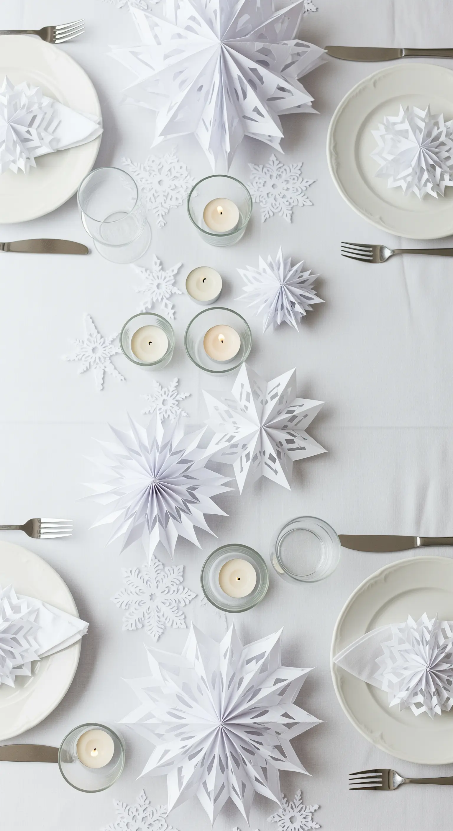 Tavola natalizia total white decorata con stelle e fiocchi di neve di carta.