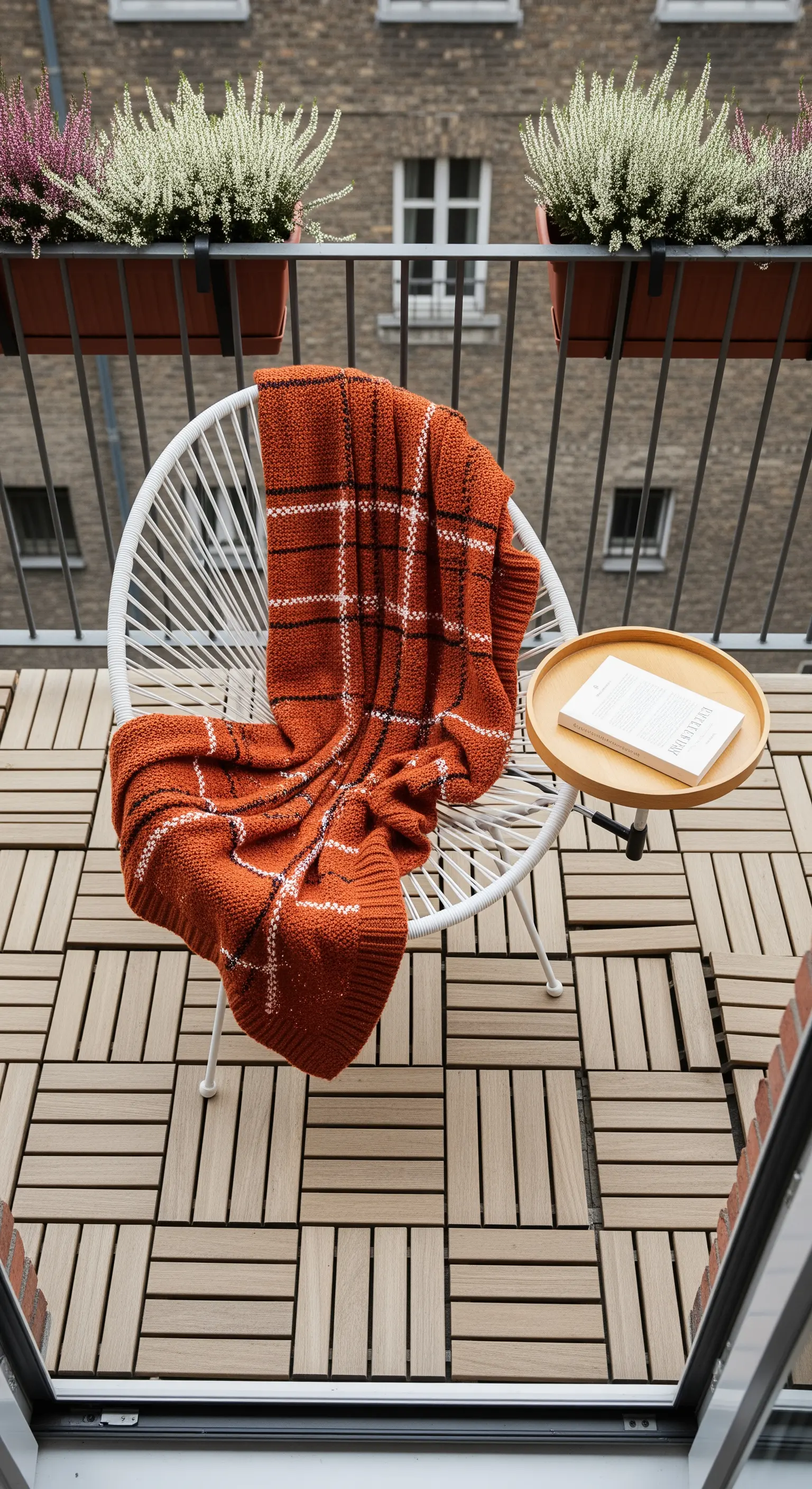 Sedia bianca di design su un piccolo balcone con pavimento a listelli e un plaid arancione.