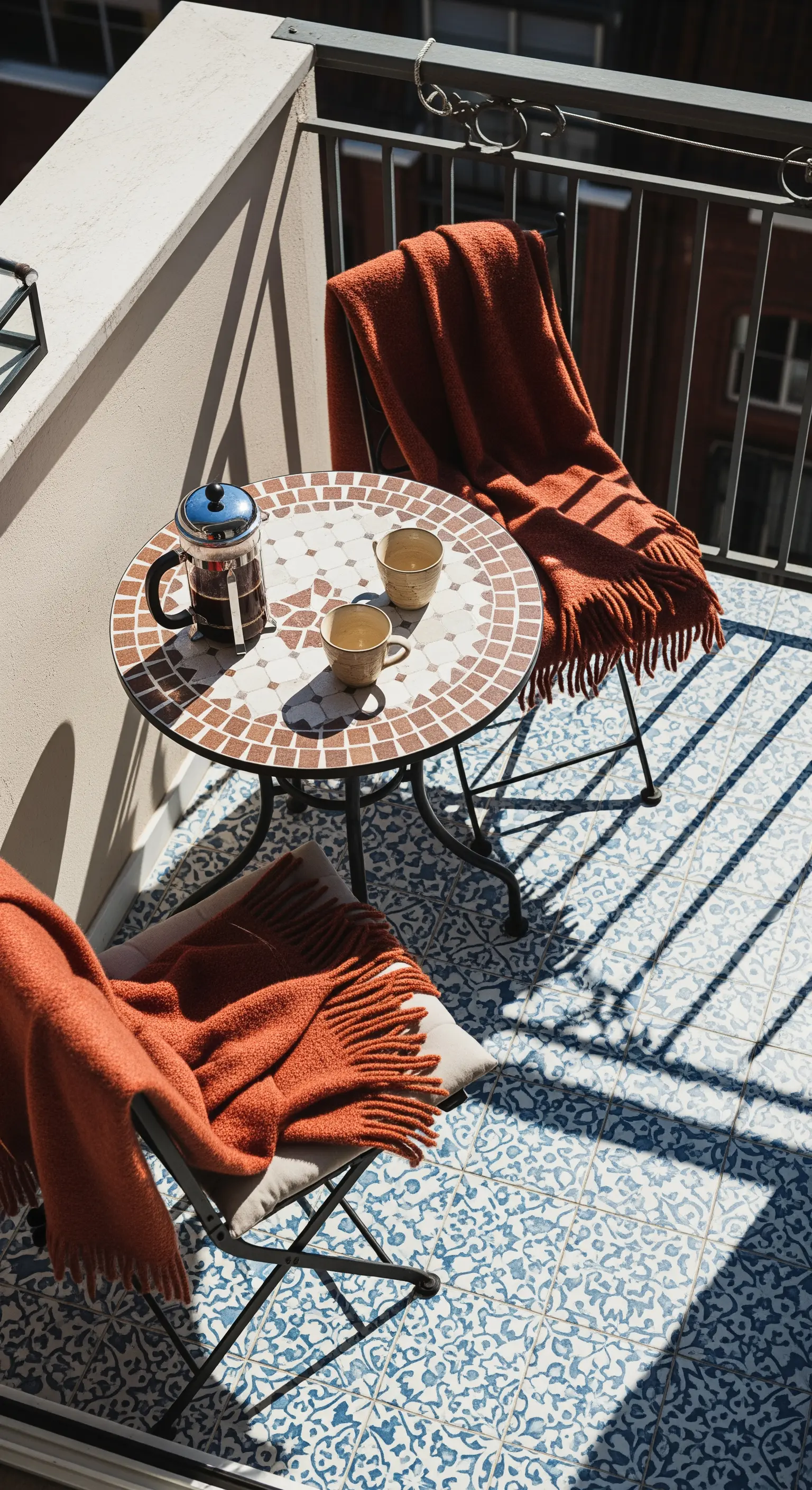 Balcone con piastrelle decorate blu e bianche, tavolino a mosaico e coperte color ruggine.