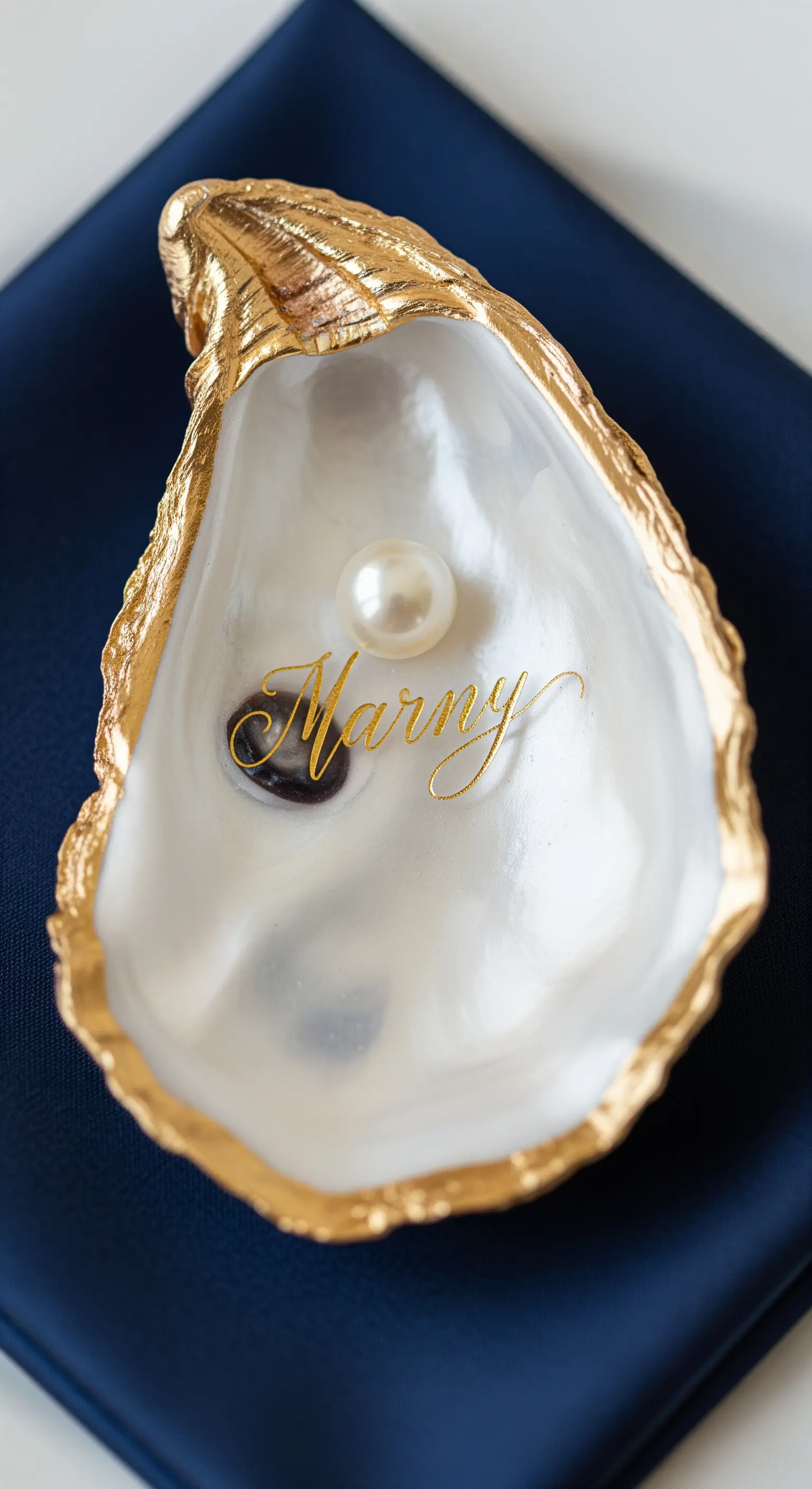 Guscio d'ostrica dorato con una perla all'interno e un nome calligrafato in oro.