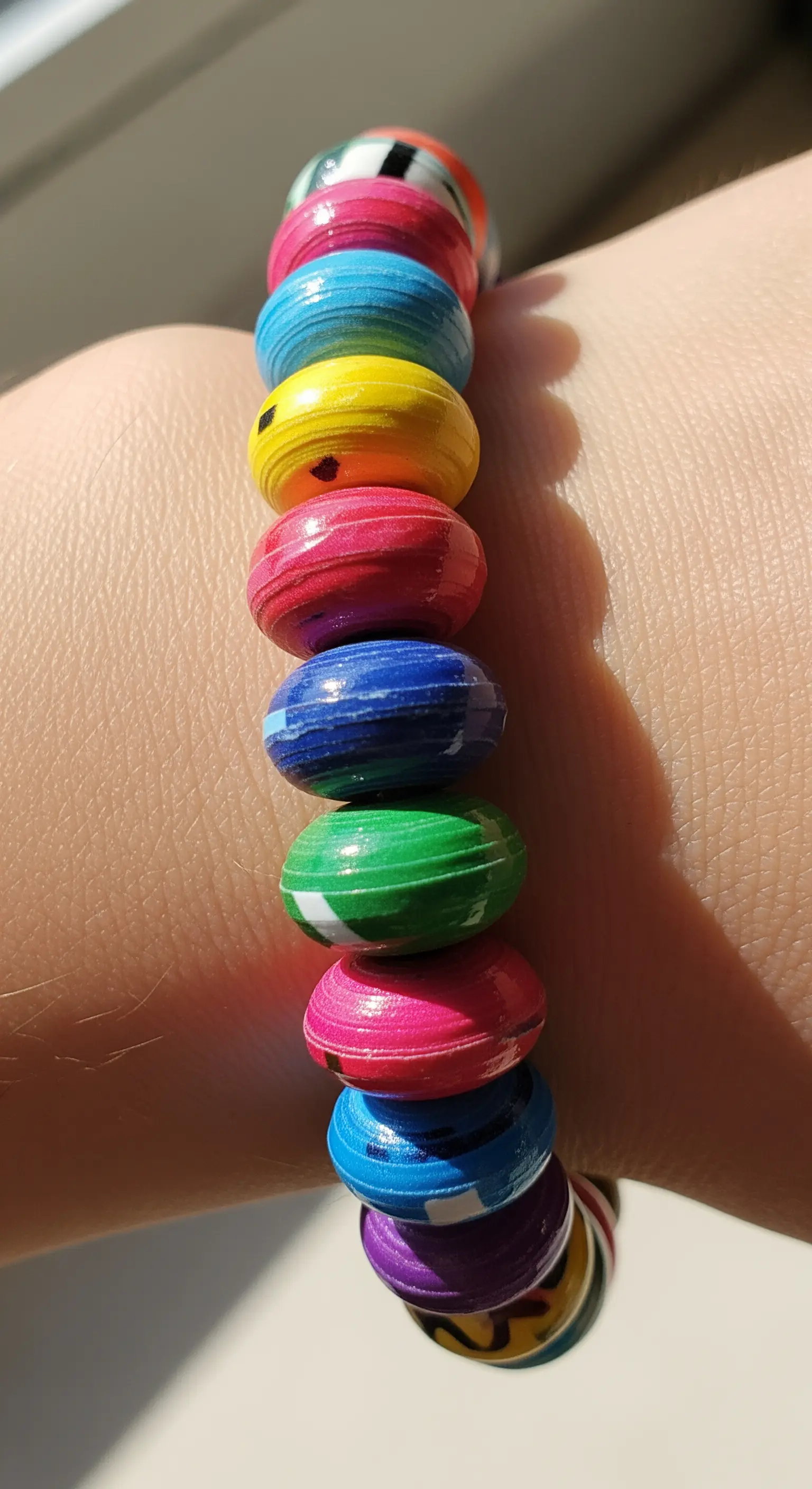 Un braccialetto elastico composto da perline colorate realizzate arrotolando carta di riviste riciclata.