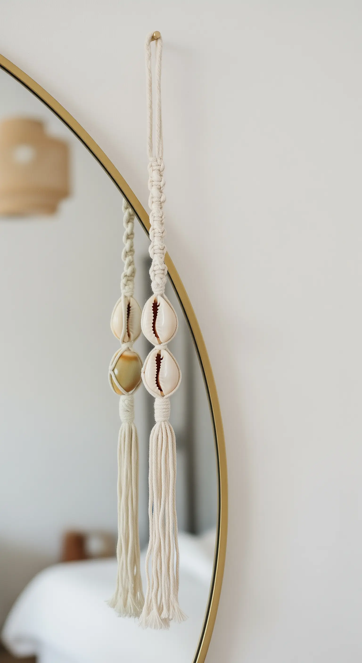 Piccola decorazione in macramè con conchiglie ciprea appesa al bordo di uno specchio dorato.