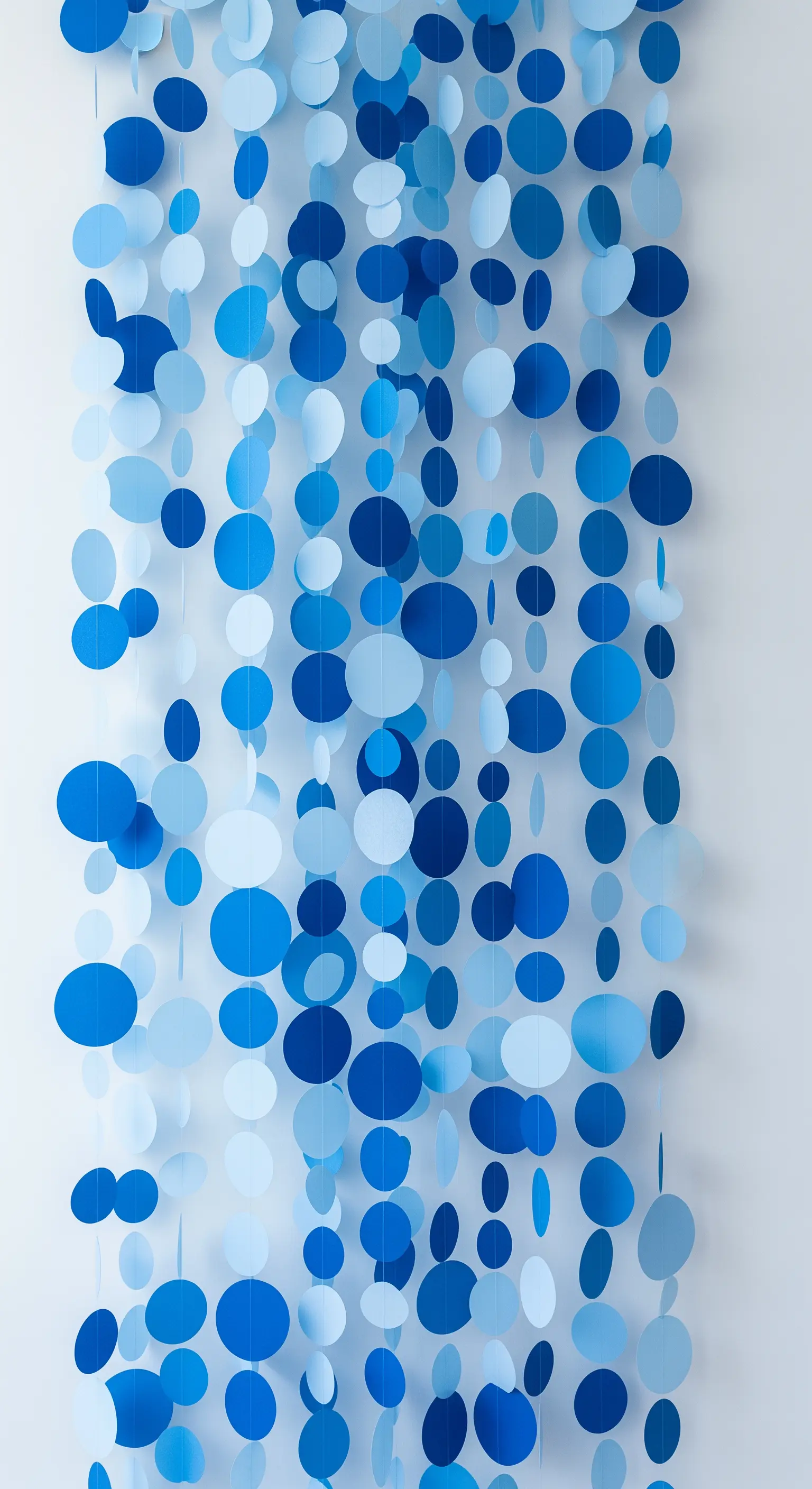 Ghirlande verticali composte da cerchi di carta in diverse tonalità di blu, appese a creare una tenda.