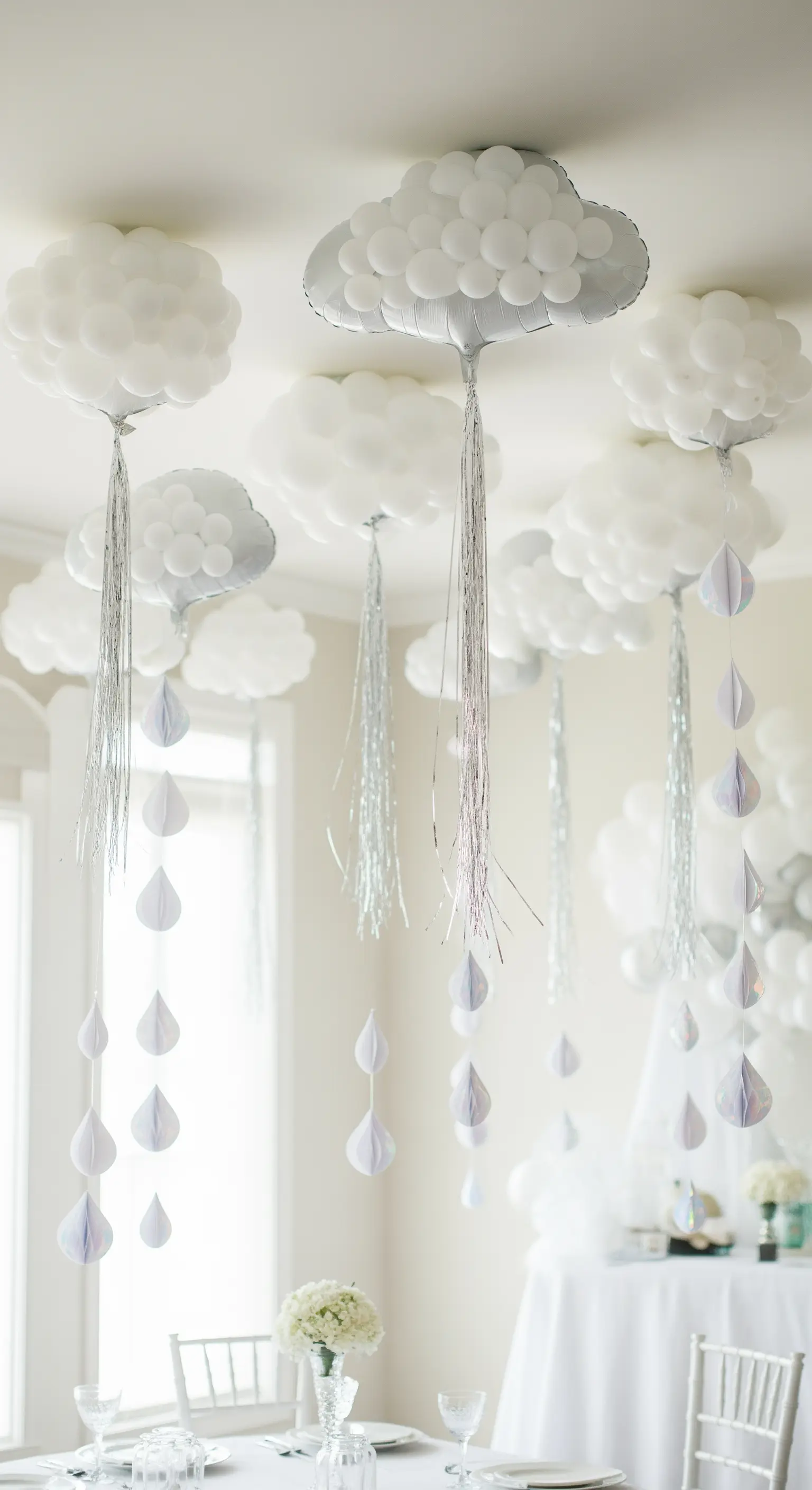 Palloncini a forma di nuvola con gocce di carta e fili argentati pendenti sopra un tavolo.