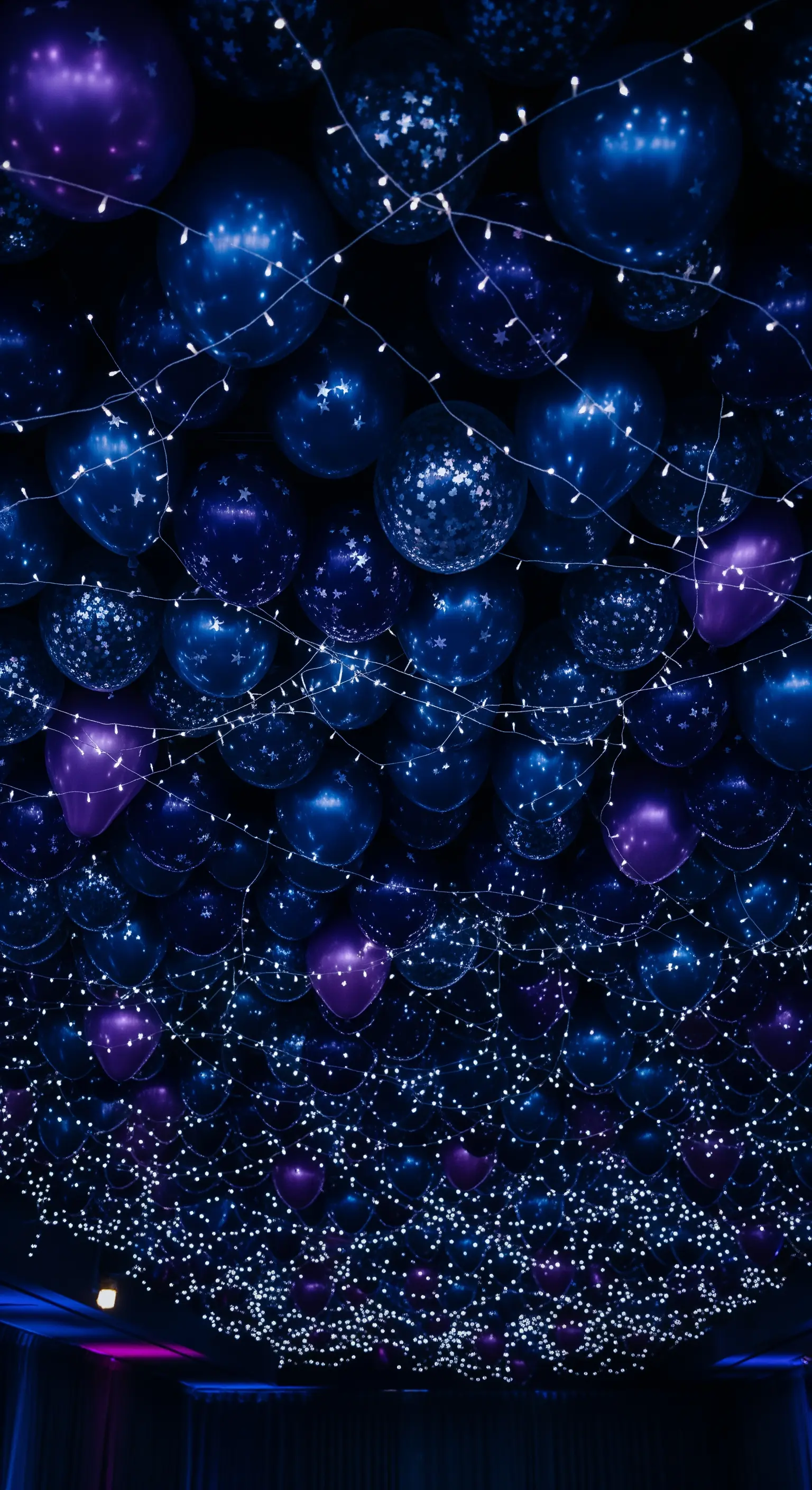 Un soffitto scuro coperto da palloncini blu e viola con stelle e fili di lucine.