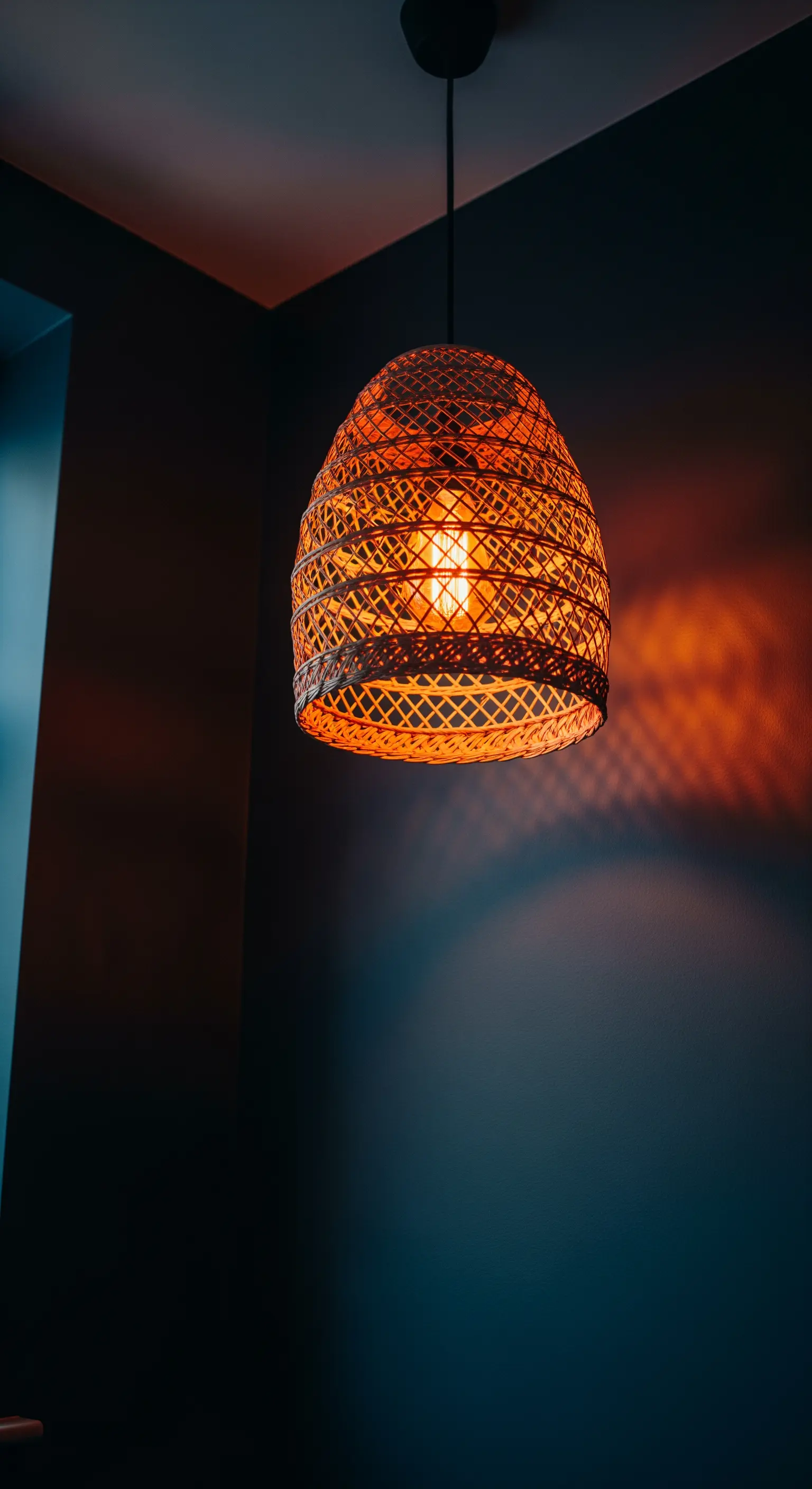 Piccolo lampadario in vimini che proietta ombre su pareti scure in un angolo.