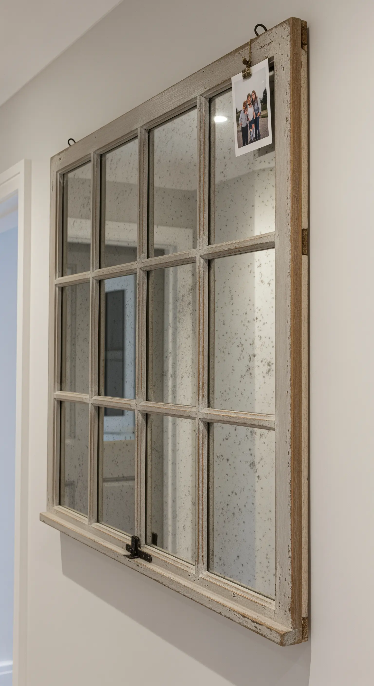Vecchia finestra in legno con vetri sostituiti da specchi anticati, appesa a una parete bianca.